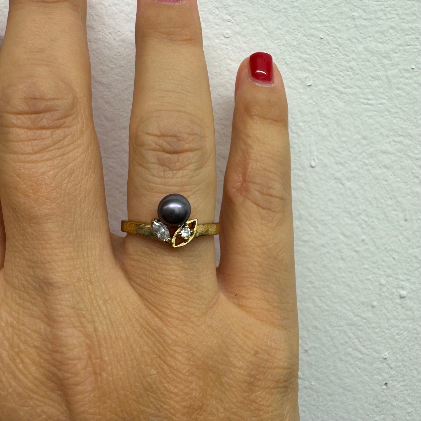 14K gold ring set with a Black Pearl at the center and clear gemstones on the sides.