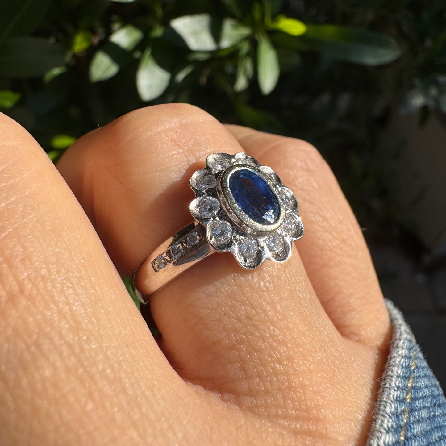 18K gold ring set with an oval blue Sapphire surrounded by a halo of round Diamonds in a flower-shaped design.