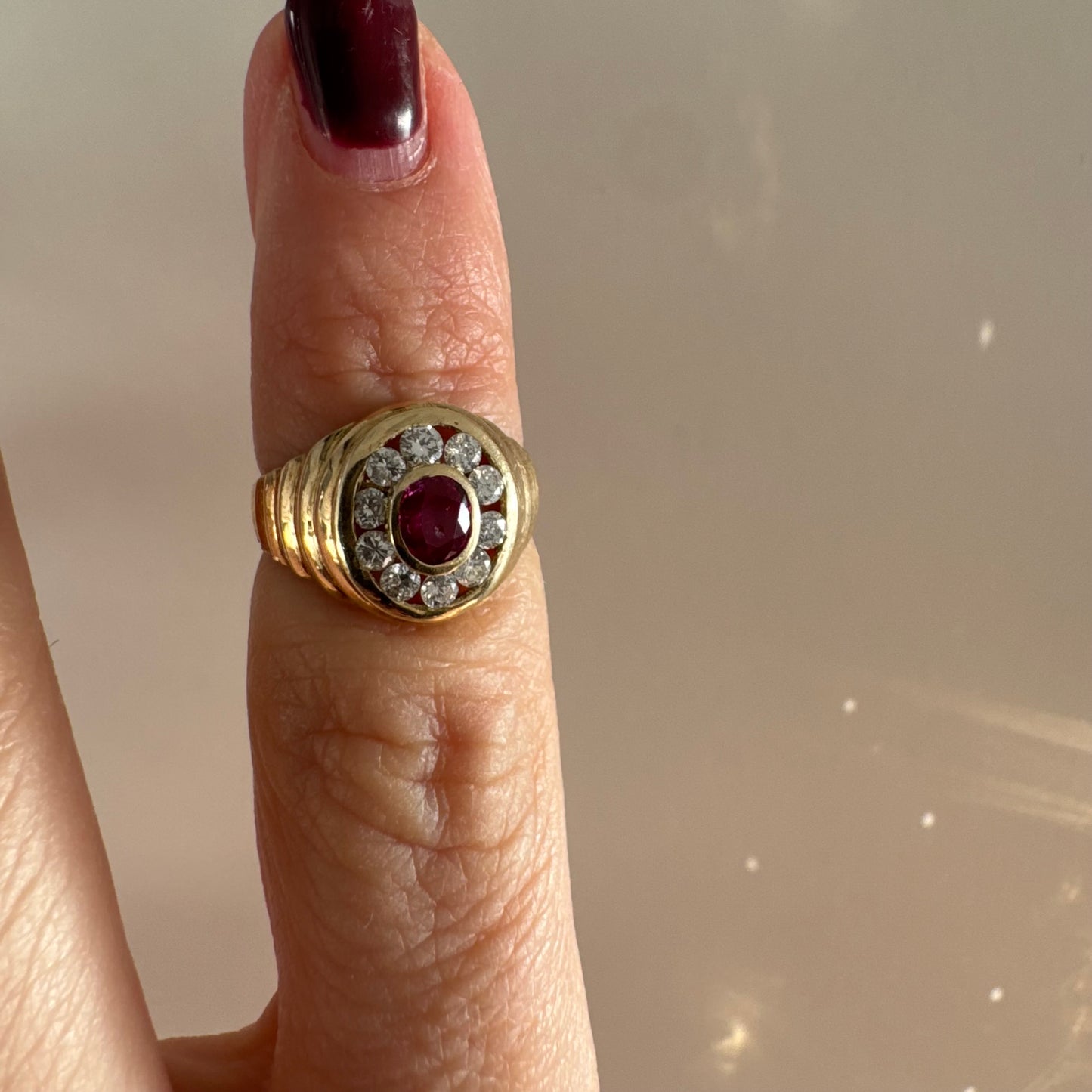 טבעת זהב צהוב 14 קראט בסגנון חותם עגול, משובצת אבן רובי מרכזית וסביבה הילה של יהלומים עגולים.