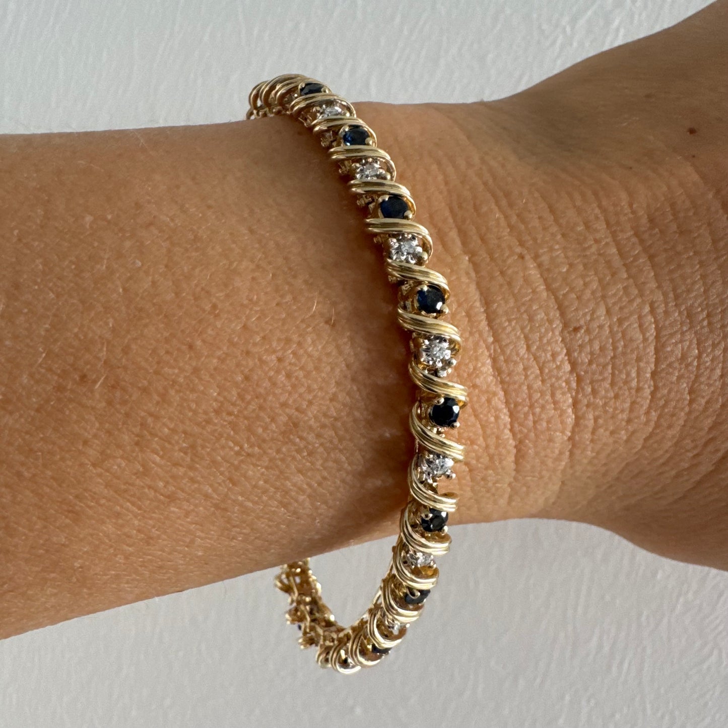 צמיד זהב צהוב 14 קראט משובץ אבני ספיר כחולות ויהלומים, המשובצים בעיצוב זורם עם קווים מעוגלים העוטפים כל אבן.