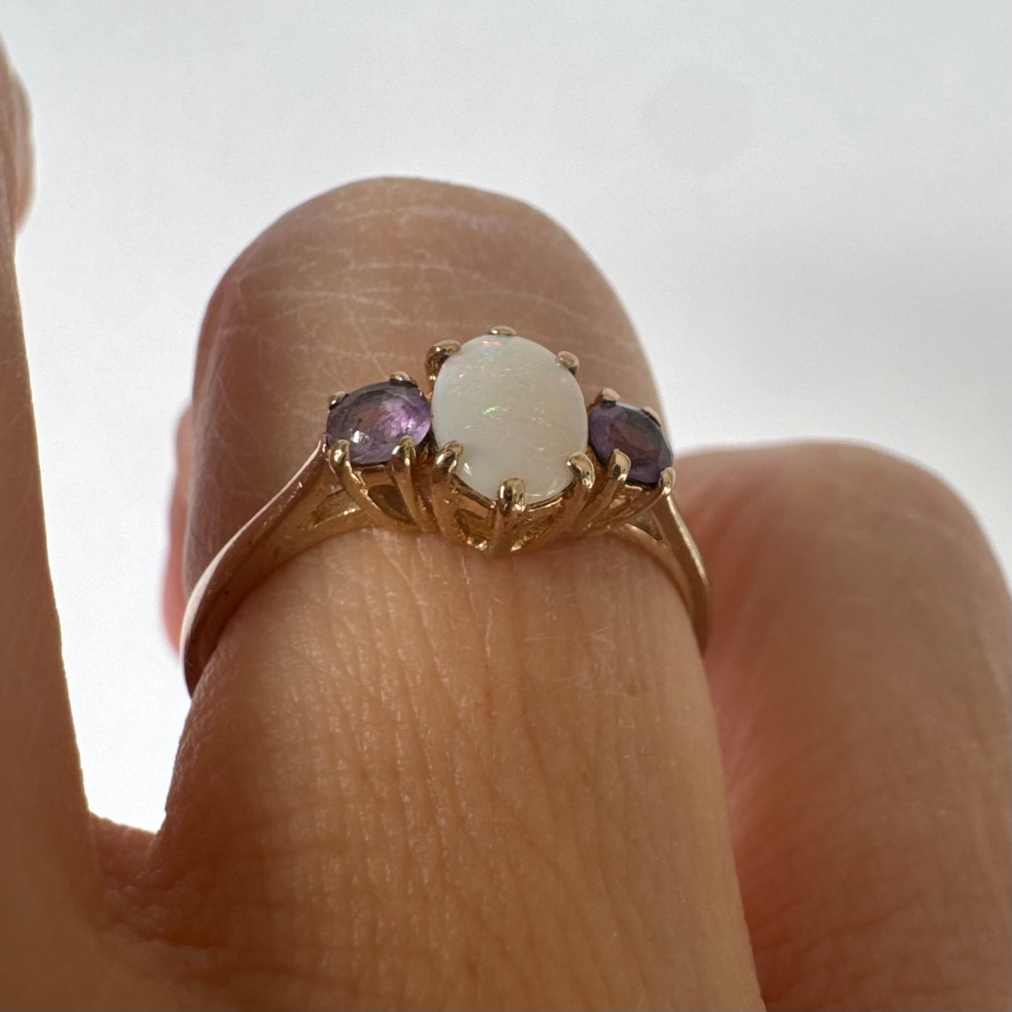 9K gold ring set with an oval Opal at the center, flanked by two delicate purple stones.