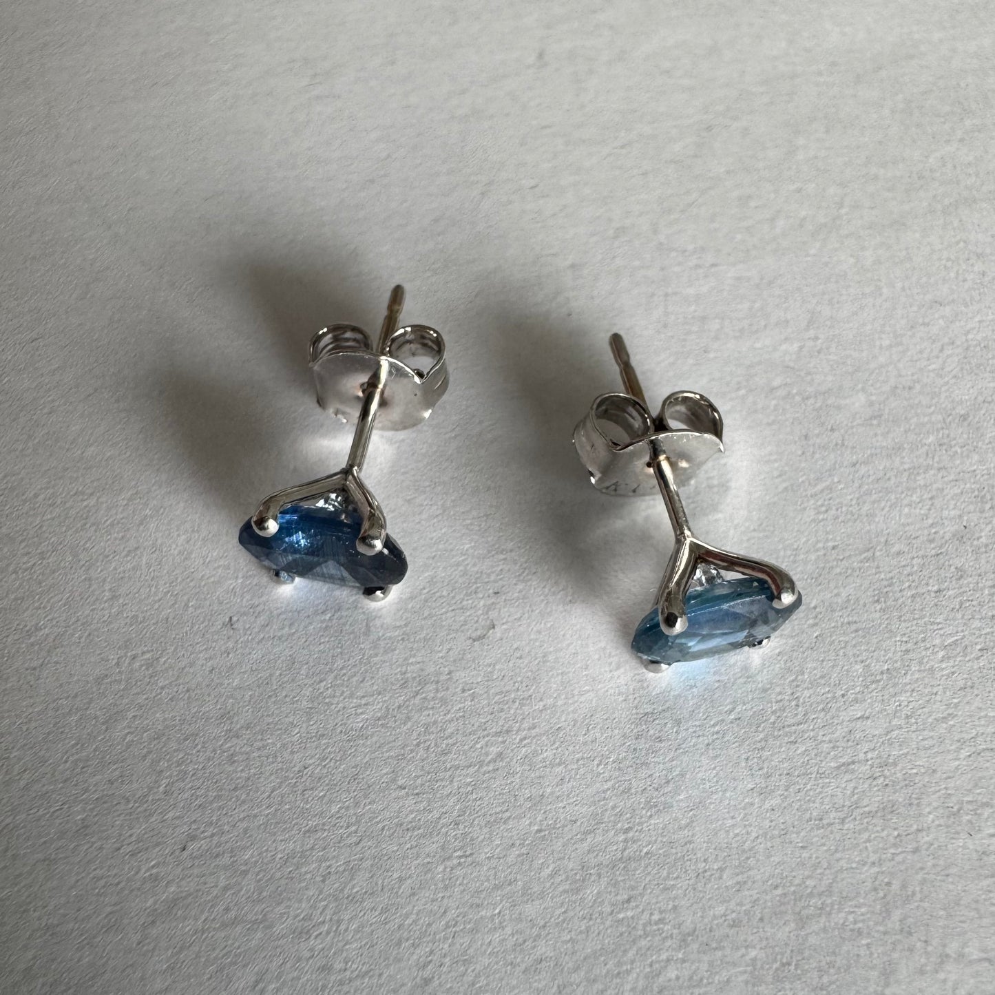 עגילי זהב לבן 14 קראט משובצים אבני טופז כחולות בחיתוך אובלי.