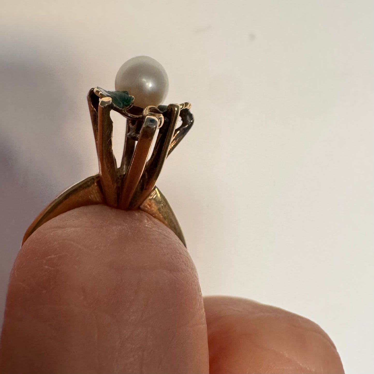 טבעת זהב 14 קראט משובצת פנינה מרכזית ומעוטרת אמייל ירוק בעבודת יד בצורת עלים.