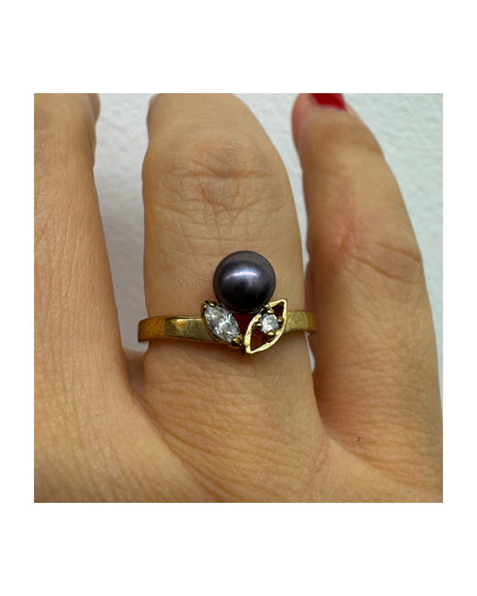 14K gold ring set with a Black Pearl at the center and clear gemstones on the sides.