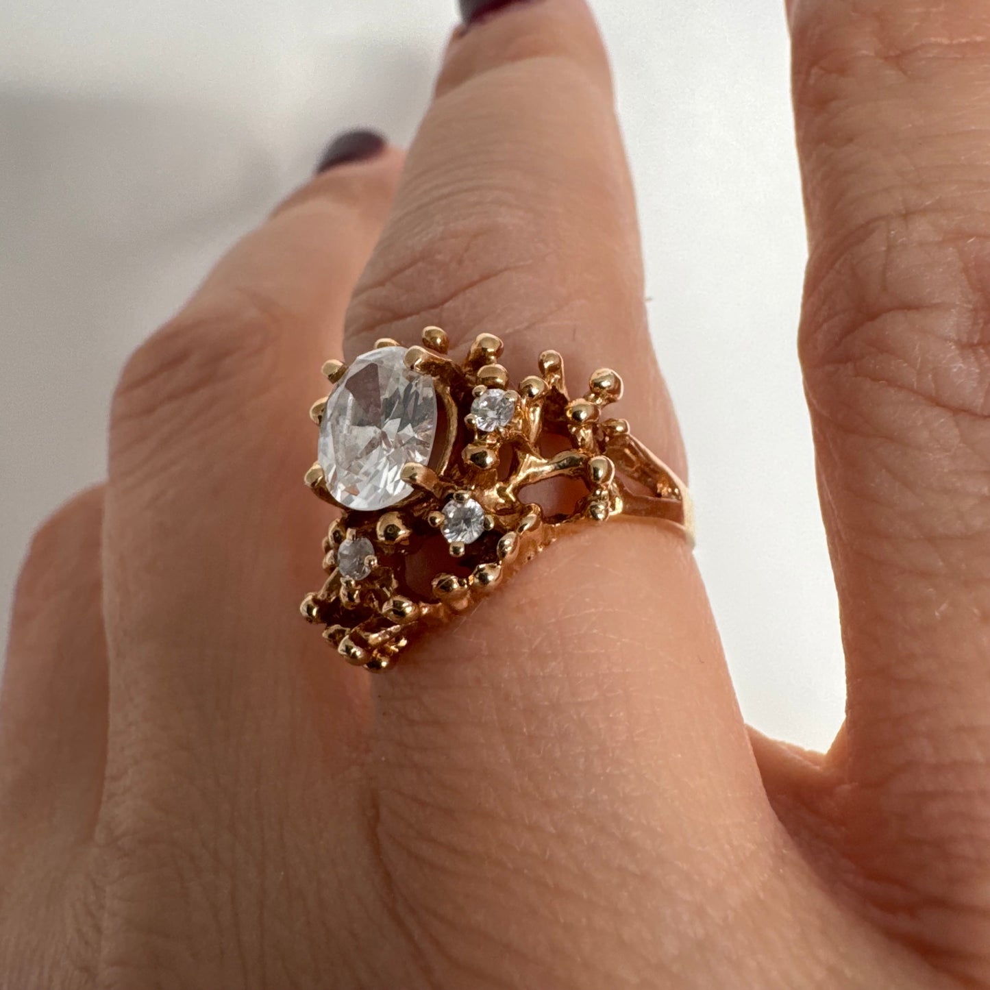 14K gold ring set with a central oval clear stone, accented by additional clear stones in an open, organic design.