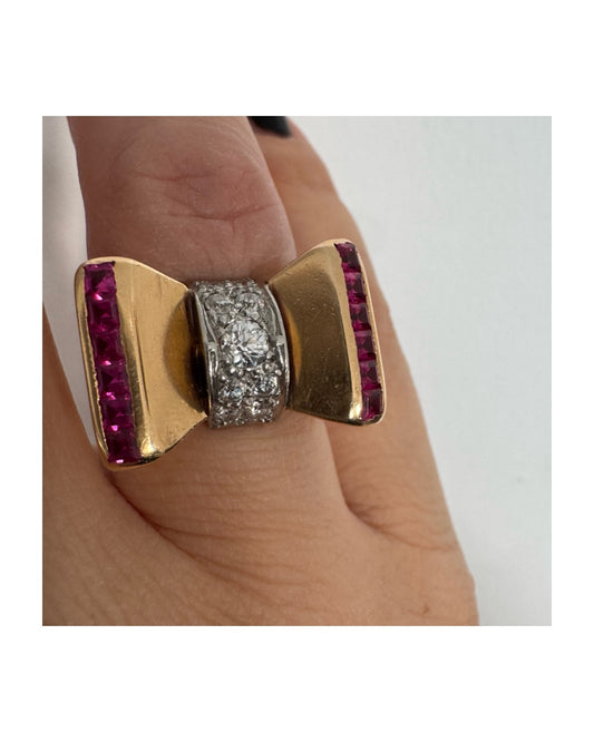 טבעת זהב 18 קראט בצורת פפיון, משובצת יהלומים במרכז ובאבני רובי בחיתוך מרובע בצדדים.