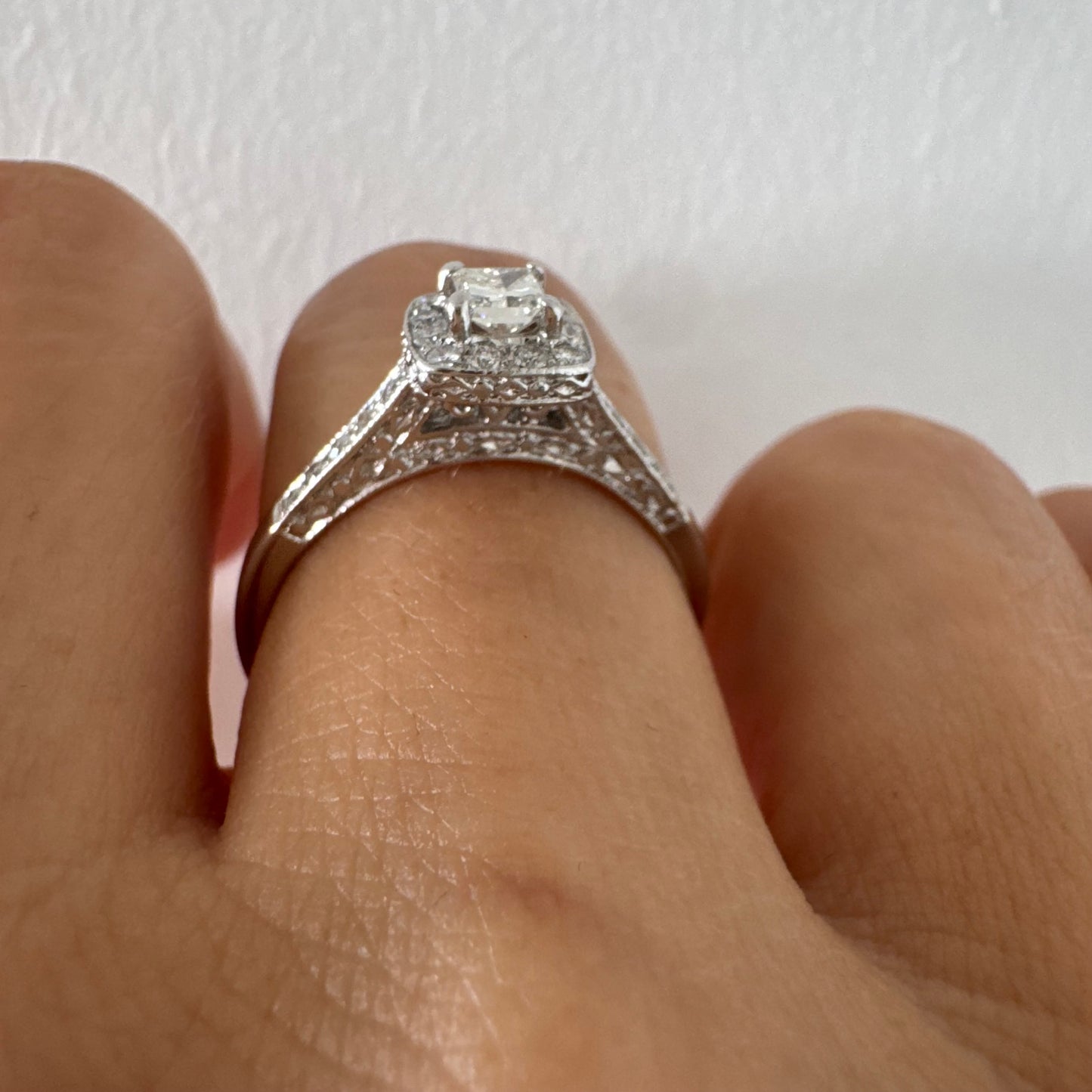 טבעת זהב לבן 14 קראט משובצת יהלום מרכזי בחיתוך פרינסס, מוקף הילת יהלומים קטנים וזרוע משובצת פאווה