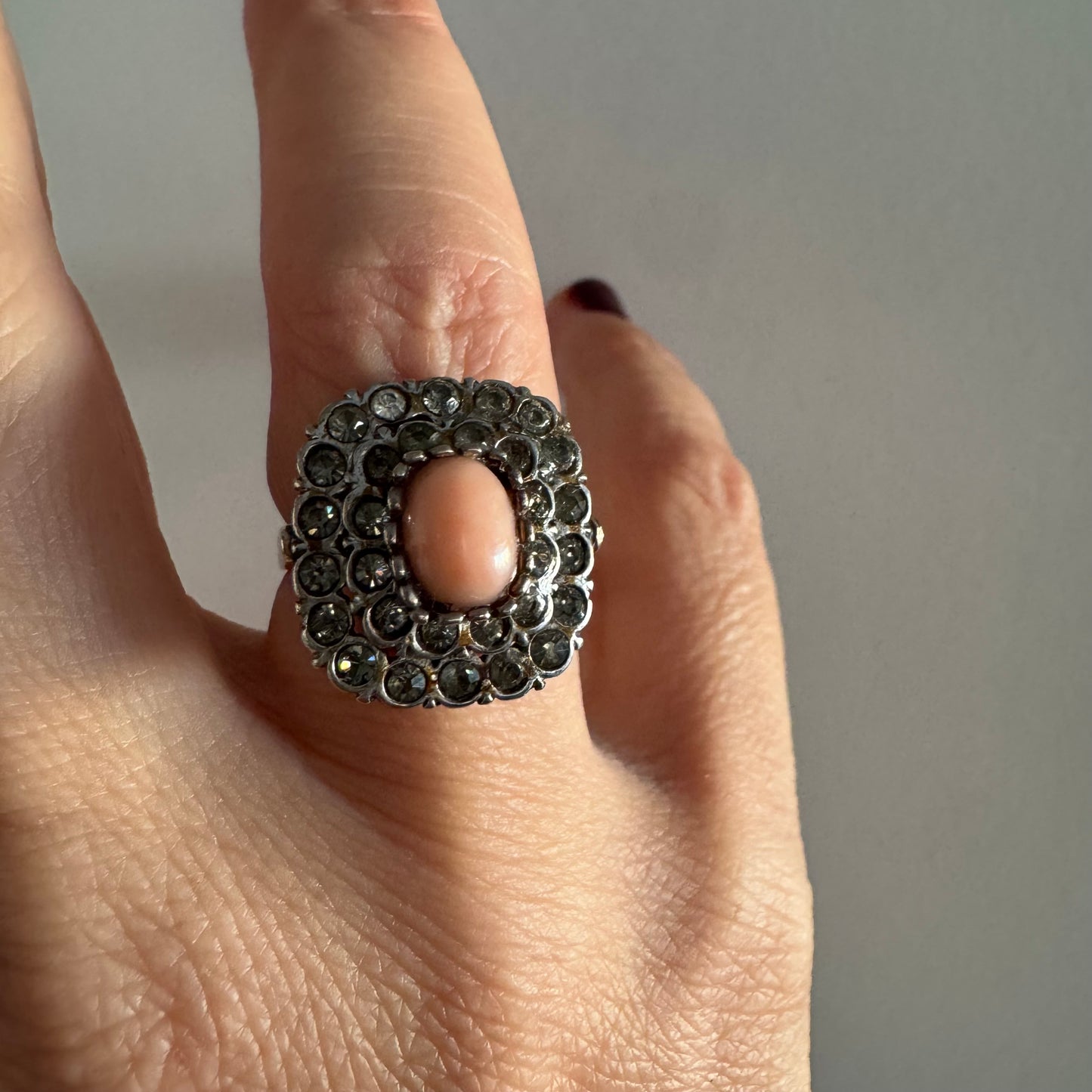 טבעת וינטג׳ עם חלק תחתון מזהב 14 קראט וחלק עליון עשוי כסף משובצת אבן קורל טבעית במרכז ומסביבה אבנים בהירות שאינן יהלומים.