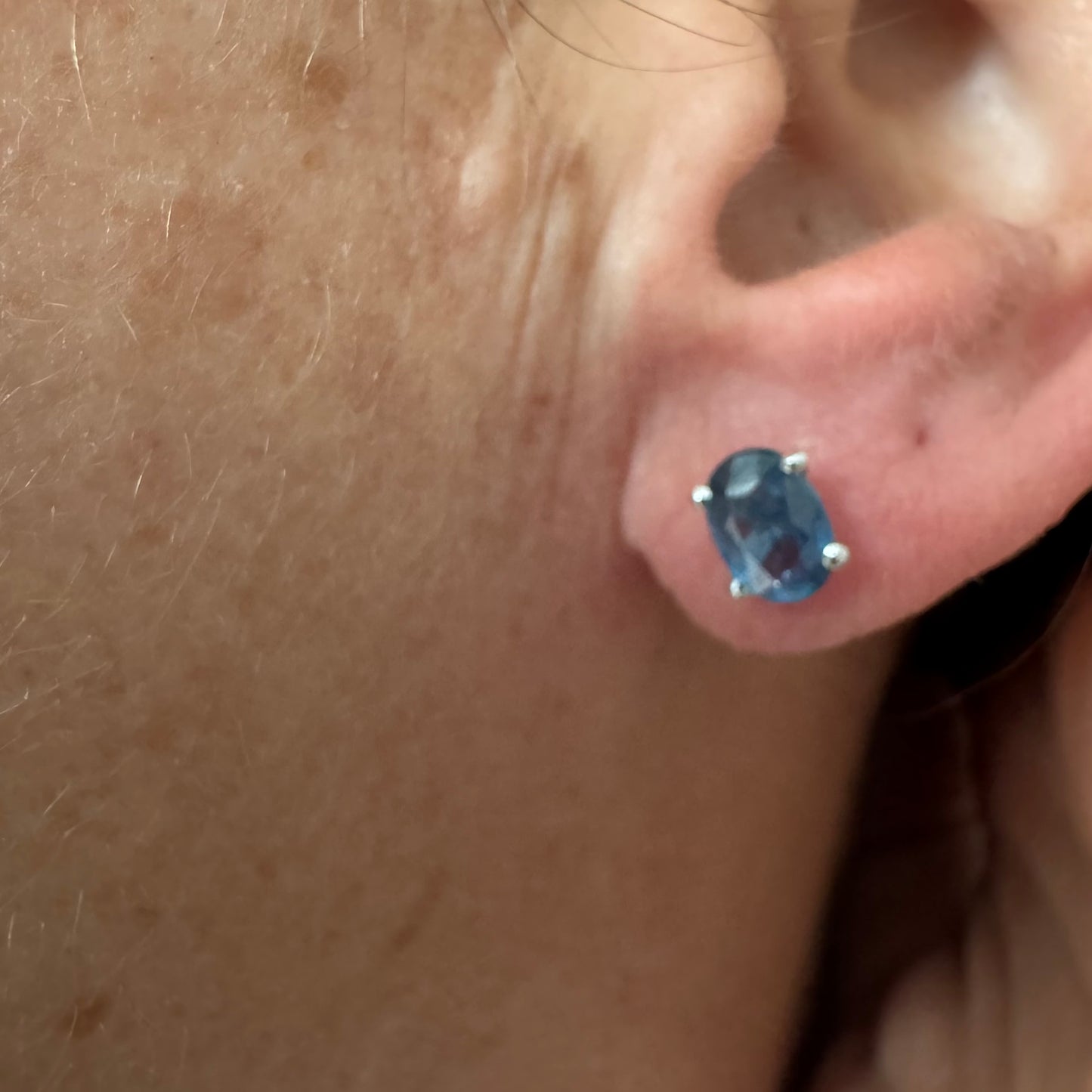 עגילי זהב לבן 14 קראט משובצים אבני טופז כחולות בחיתוך אובלי.