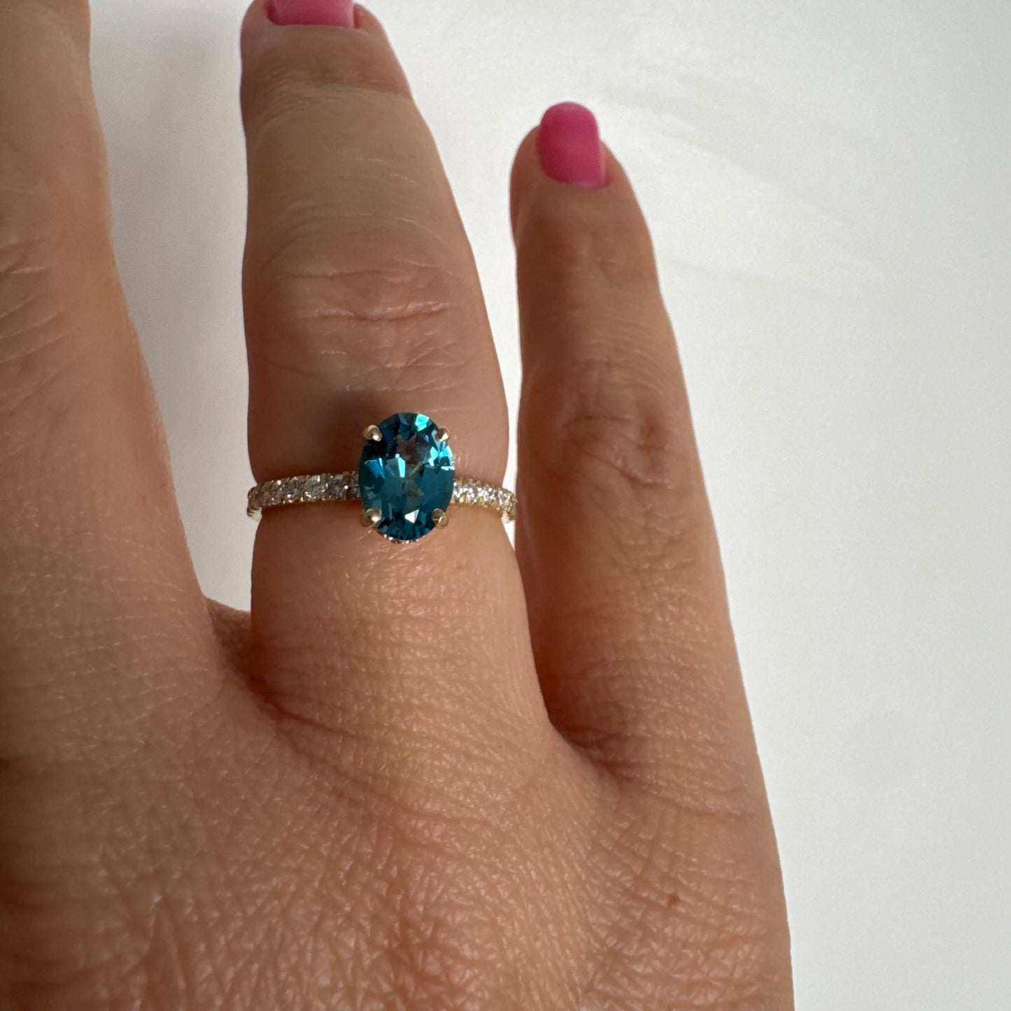 טבעת זהב צהוב 14 קראט משובצת אבן טופז כחולה אובלית בגוון טורקיז־כחול עמוק, באחיזה של ארבע שיניים עדינות ויהלומים.