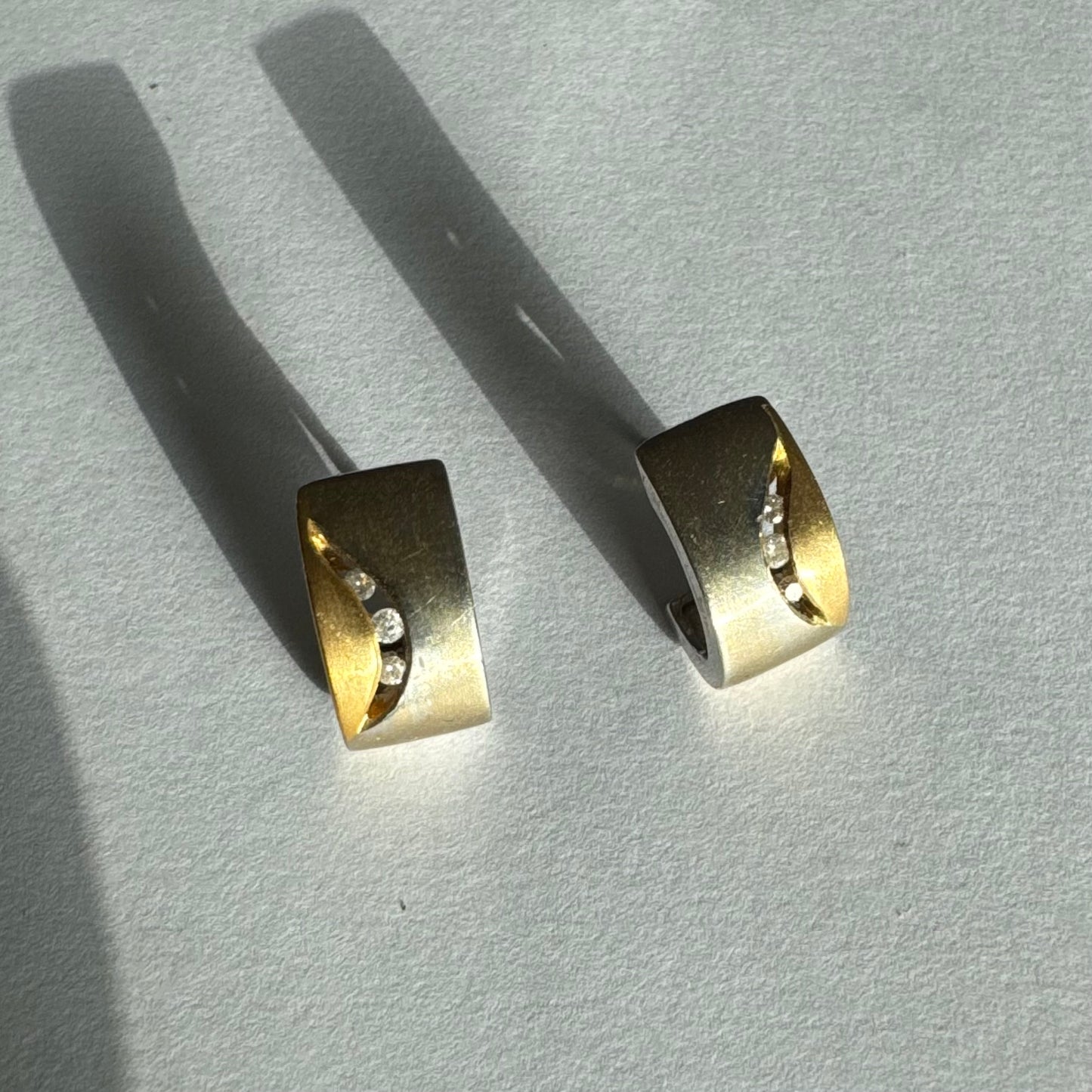 עגילי זהב 18 קראט משובצים יהלומים בעיצוב מודרני ונקי עם שילוב של שני גוונים וגימור מאט יוקרתי.