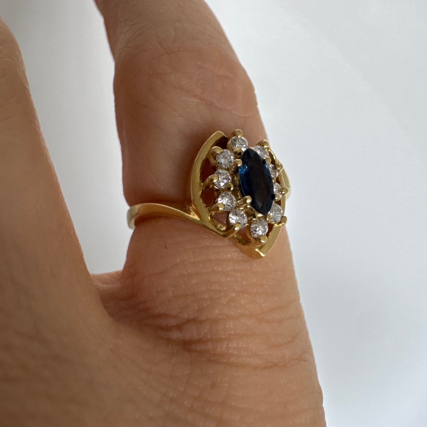 טבעת זהב צהוב 18 קראט משובצת ספיר כחול מרכזי בחיתוך מרקיזה, מוקף הילה של יהלומים המעניקים ניצוץ עדין ומדגישים את צבע האבן העמוק.