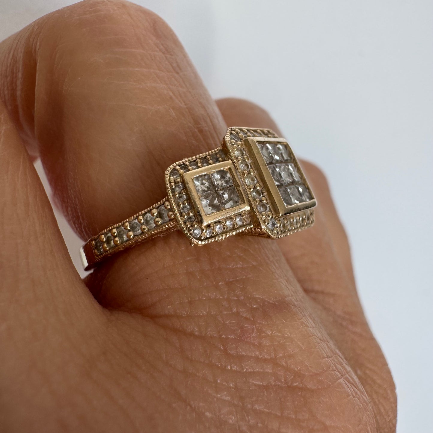 טבעת זהב צהוב 14 קראט משובצת יהלומים בחיתוך פרינסס במרכז, מוקפת הילה של יהלומים צדדיים.