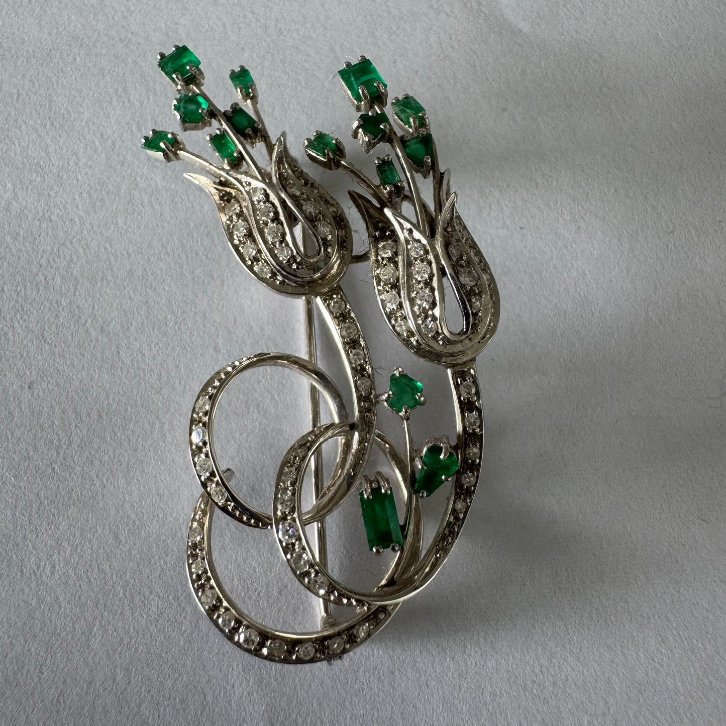 18K gold vintage brooch featuring an elegant floral design set with vibrant Emeralds and sparkling Diamonds.