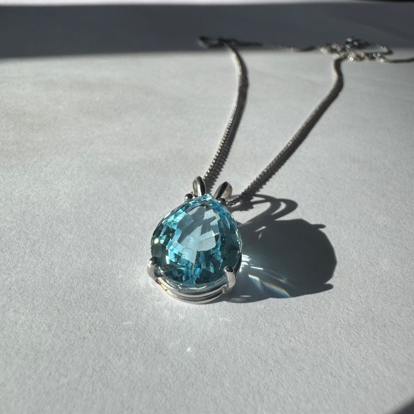 תליון זהב לבן 14 קראט המשובץ אבן טופז כחולה בחיתוך טיפה.