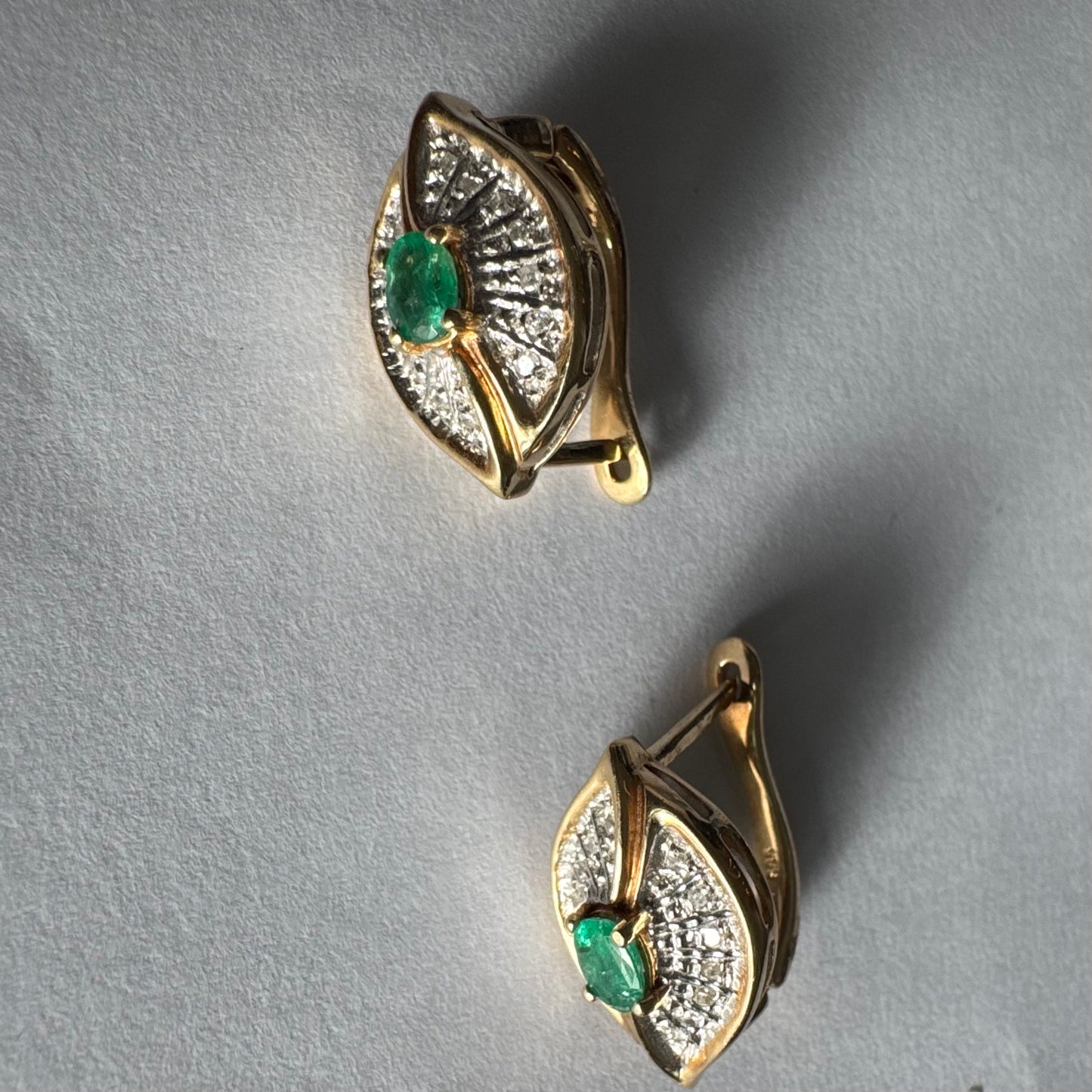 עגילים צמודים לאוזן, זהב צהוב 14 קראט, משובצים אמרלד במרכז, וסביבן פיתוחים משובצים יהלומים, שמעניקים מראה של ניצוץ רך ואלגנטי