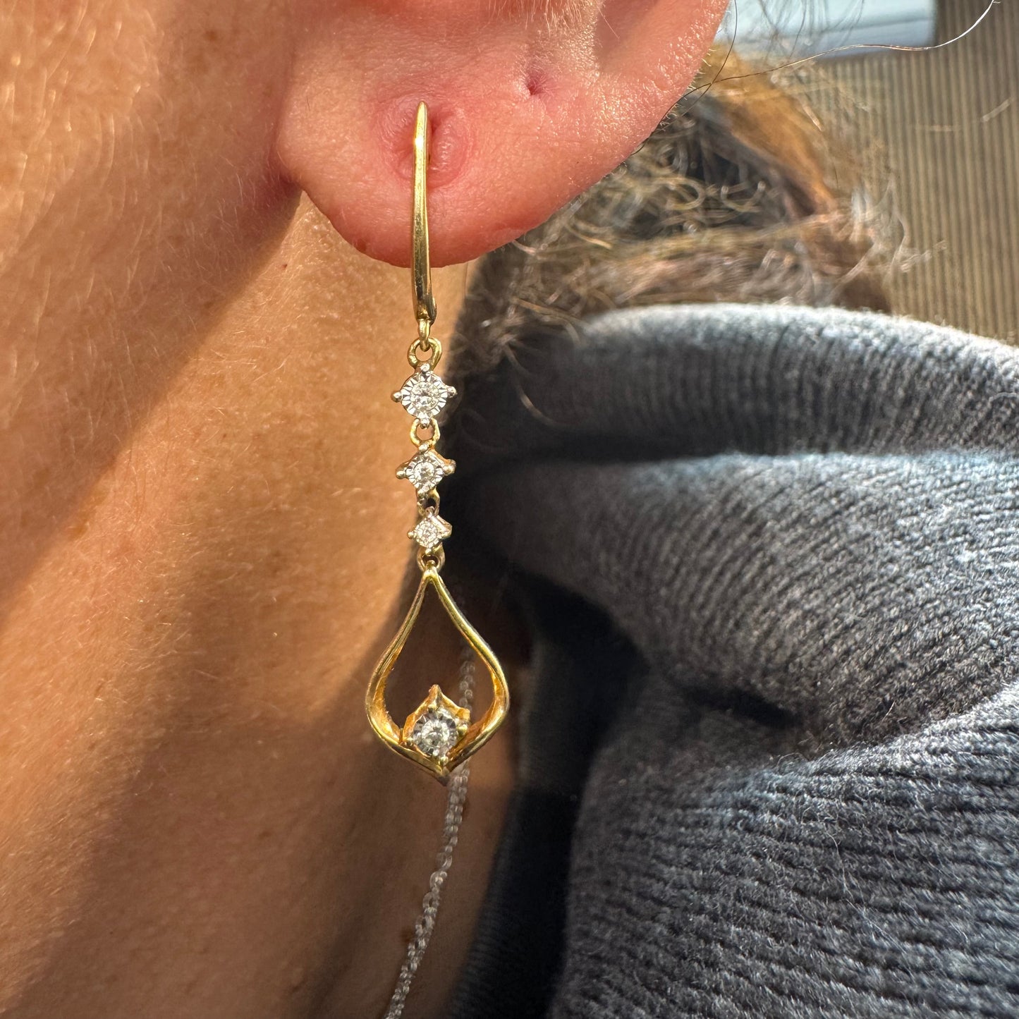 עגילי זהב 14 קראט תלויים בעיצוב עדין ומודרני, משובצים יהלומים לבנים לאורך החלק המרכזי ובטיפה פתוחה בתחתית משובץ יהלום נוסף.