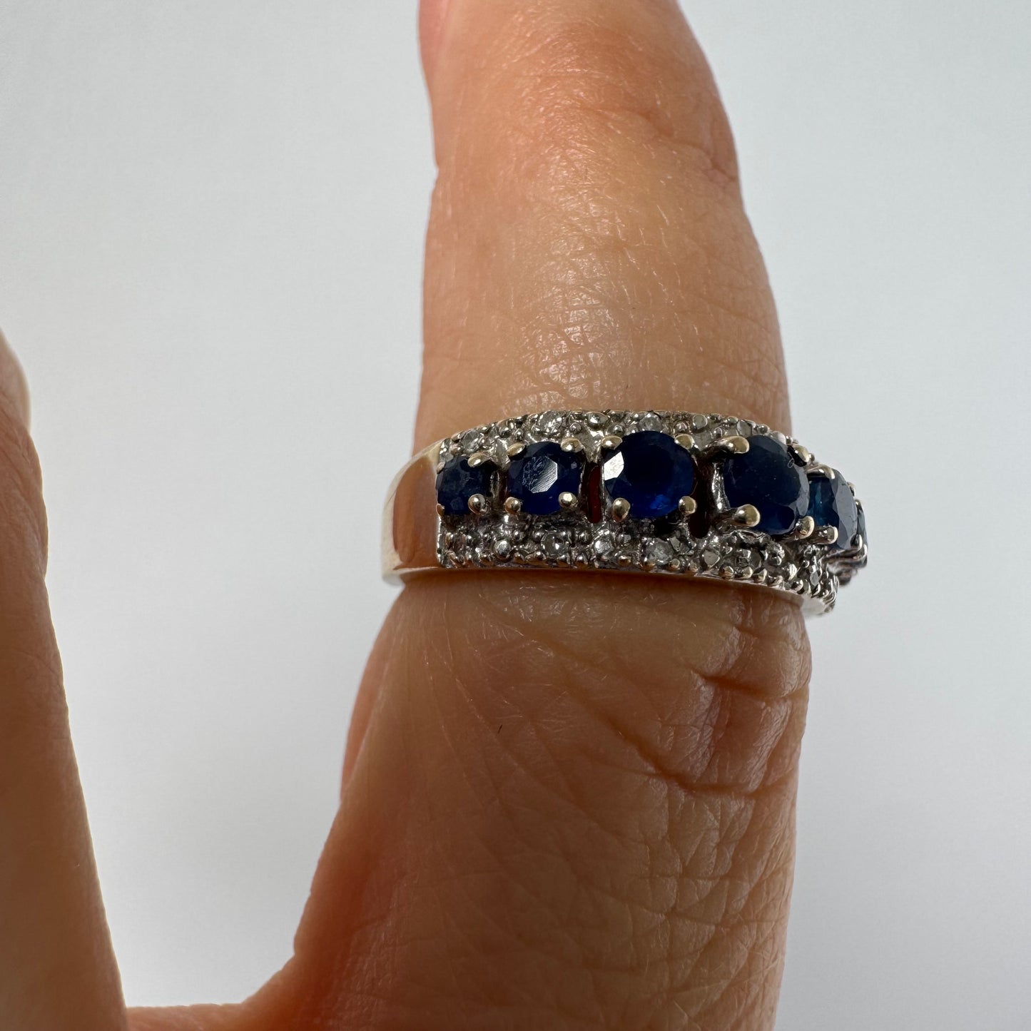 18K gold ring set with deep blue sapphires in a classic round cut, framed by two shimmering rows of brilliant Diamonds.