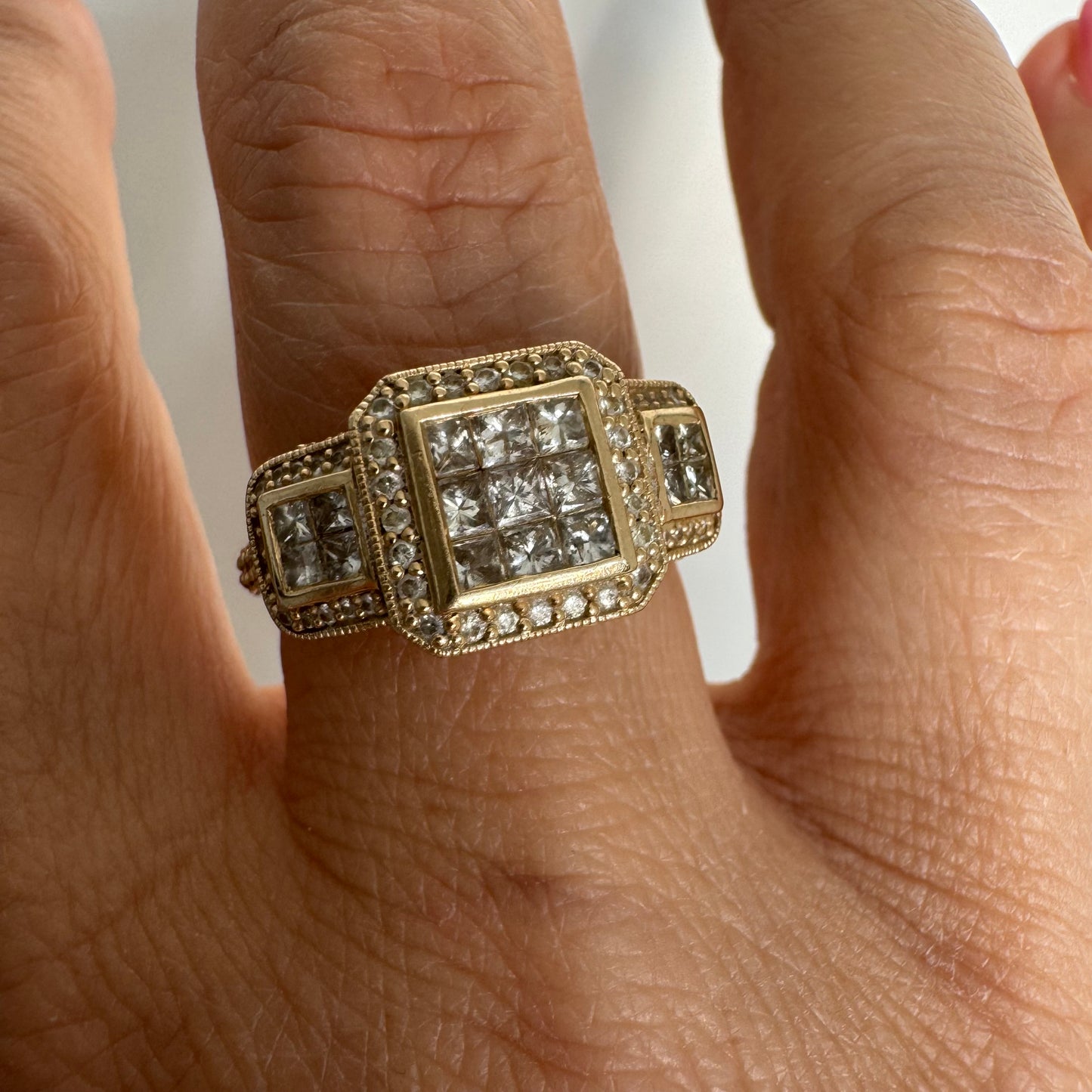 טבעת זהב צהוב 14 קראט משובצת יהלומים בחיתוך פרינסס במרכז, מוקפת הילה של יהלומים צדדיים.