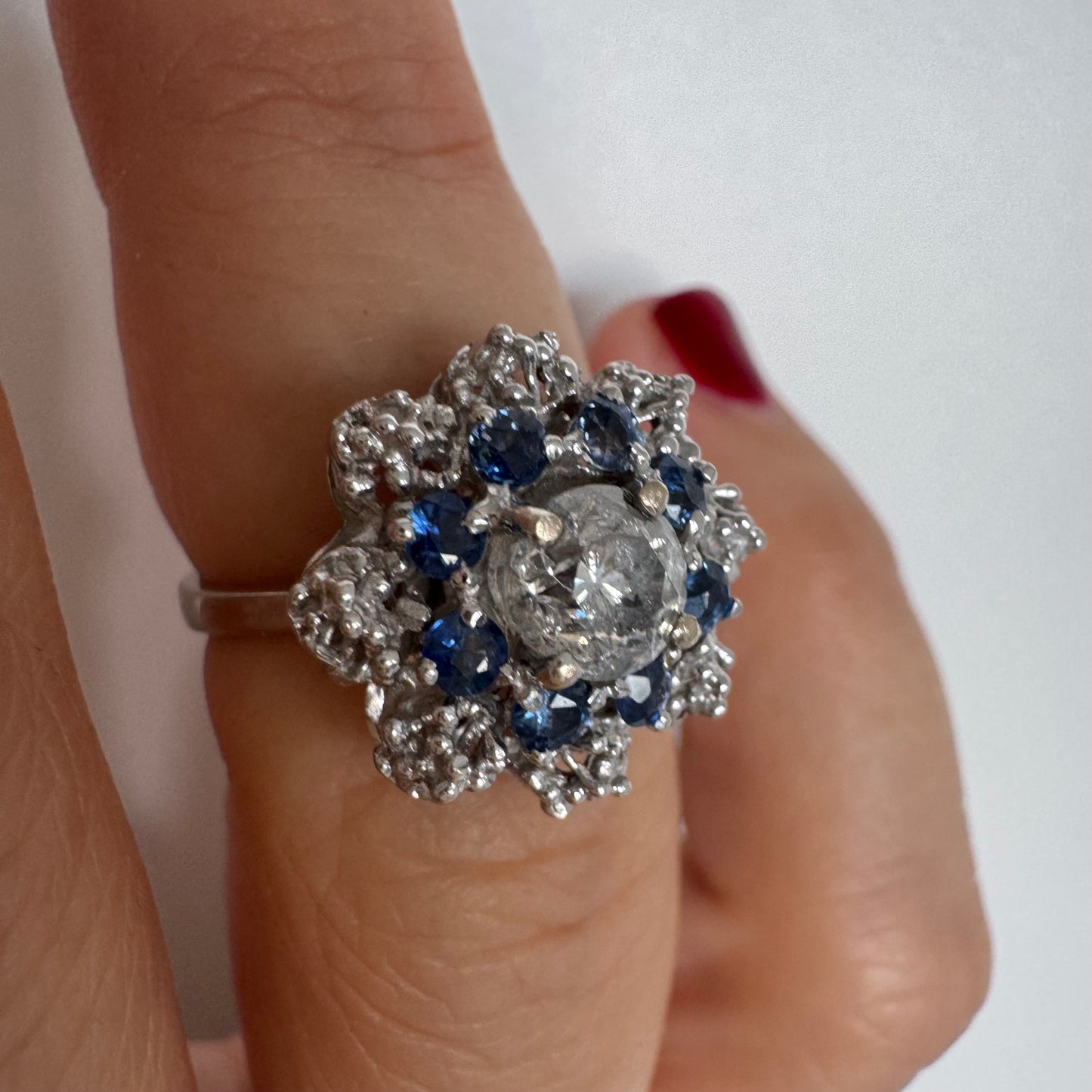 18K gold ring featuring a large round Diamond at the center, surrounded by a floral halo of purple -blue Tanzanite and & Diamonds.