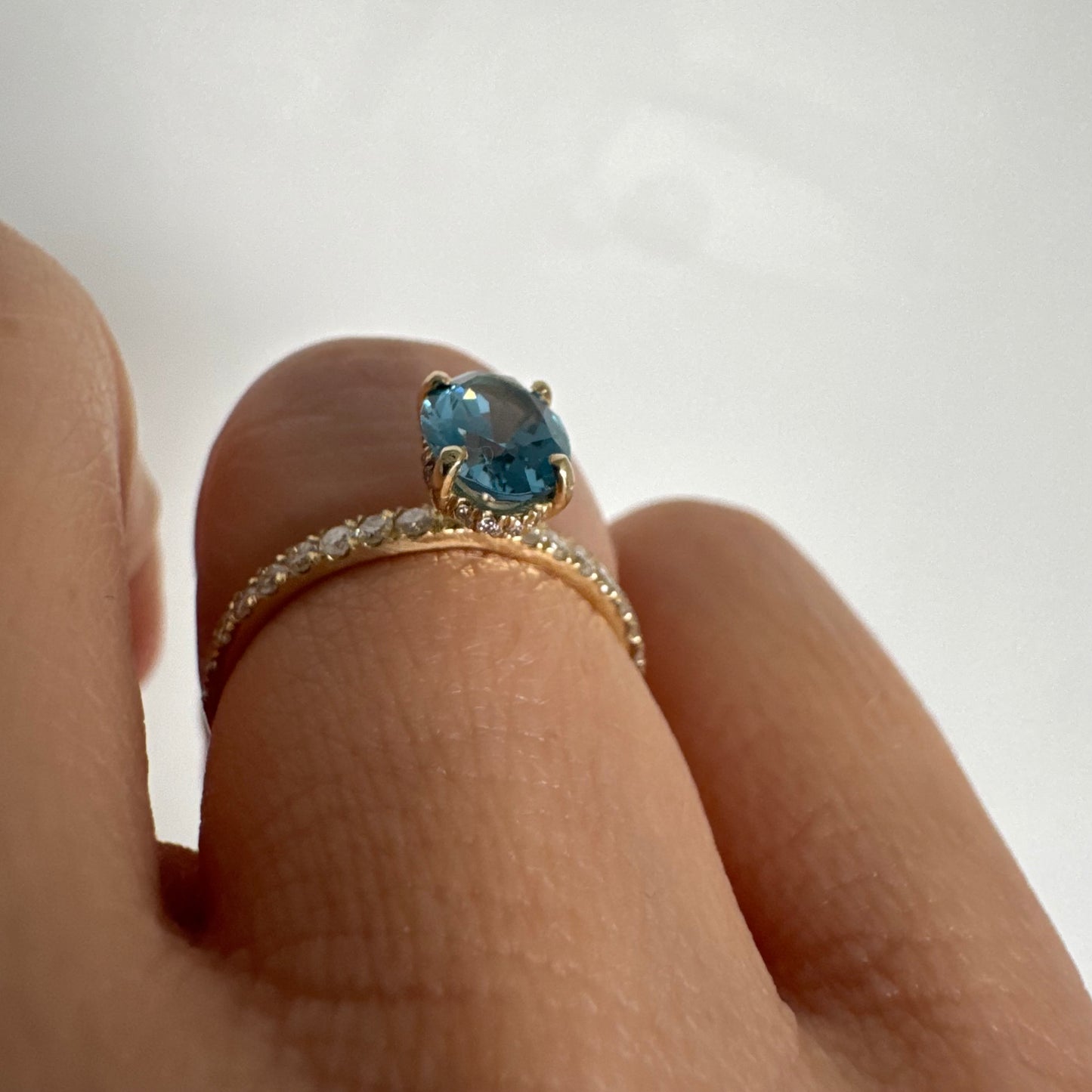 טבעת זהב צהוב 14 קראט משובצת אבן טופז כחולה אובלית בגוון טורקיז־כחול עמוק, באחיזה של ארבע שיניים עדינות ויהלומים.