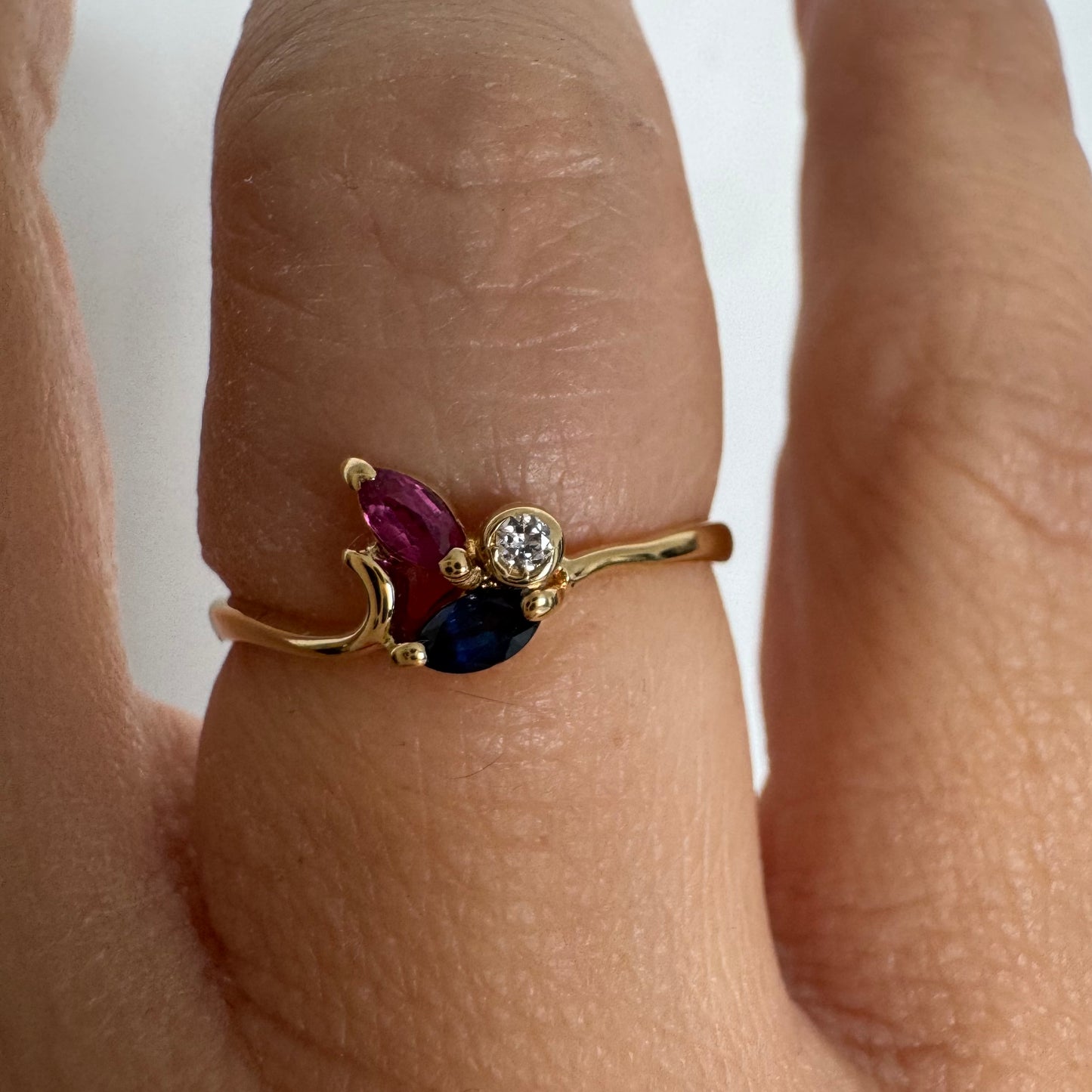 Delicate 18K gold ring set with pink and blue Sapphires alongside a sparkling center stone.