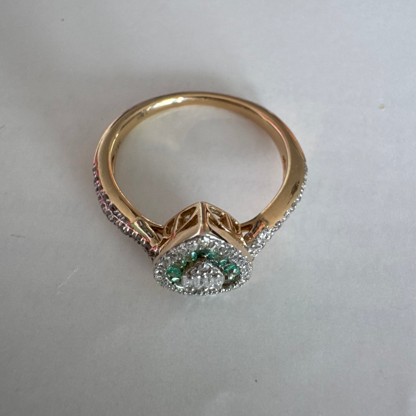 טבעת זהב צהוב 14 קראט בעיצוב טיפה (pear shape), משובצת יהלומים לבנים בשיבוץ הילה כפולה (double halo) ואבני אמרלד קטנות המקיפות מרכז ייחודי של יהלומים בחיתוך באגט