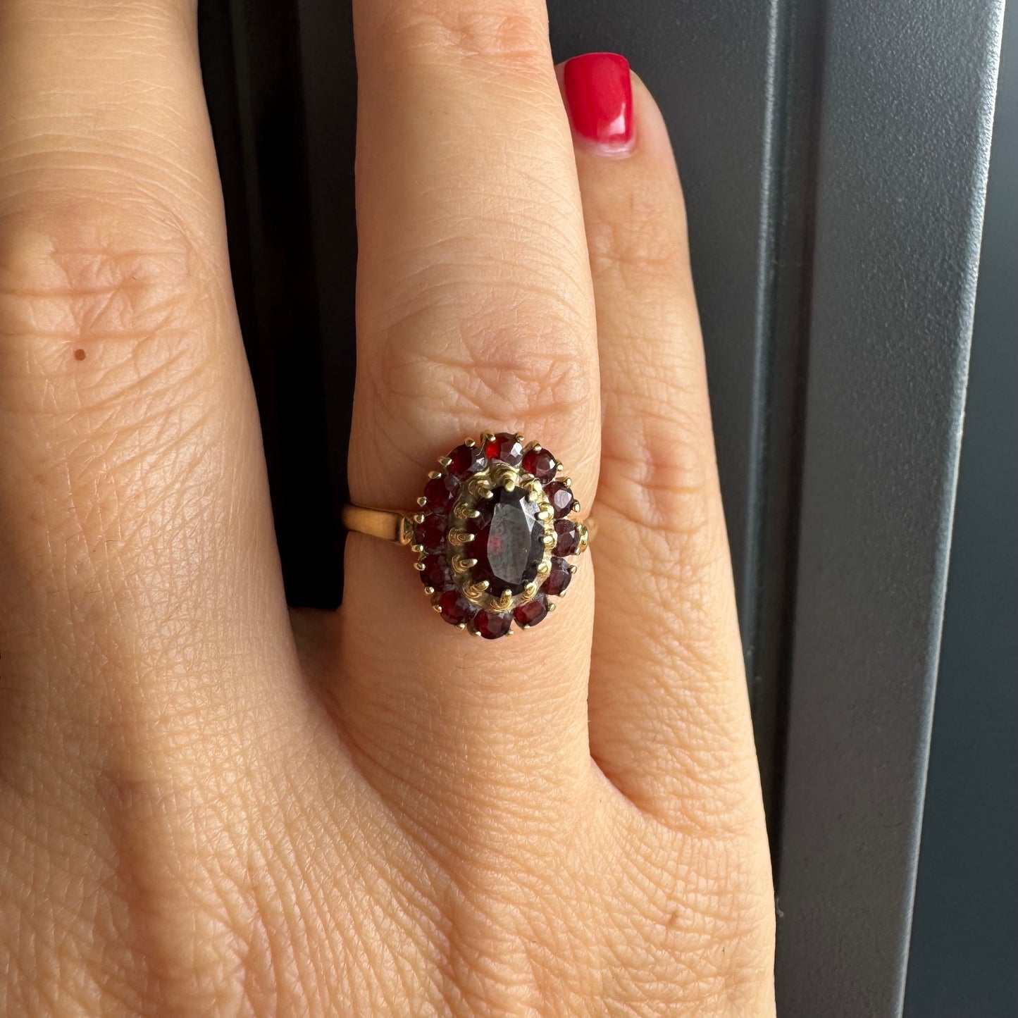 טבעת זהב צהוב 18 קראט משובצת אבן גרנט אובלית במרכז, מוקפת באבני גרנט קטנות בסידור אליפטי קלאסי.