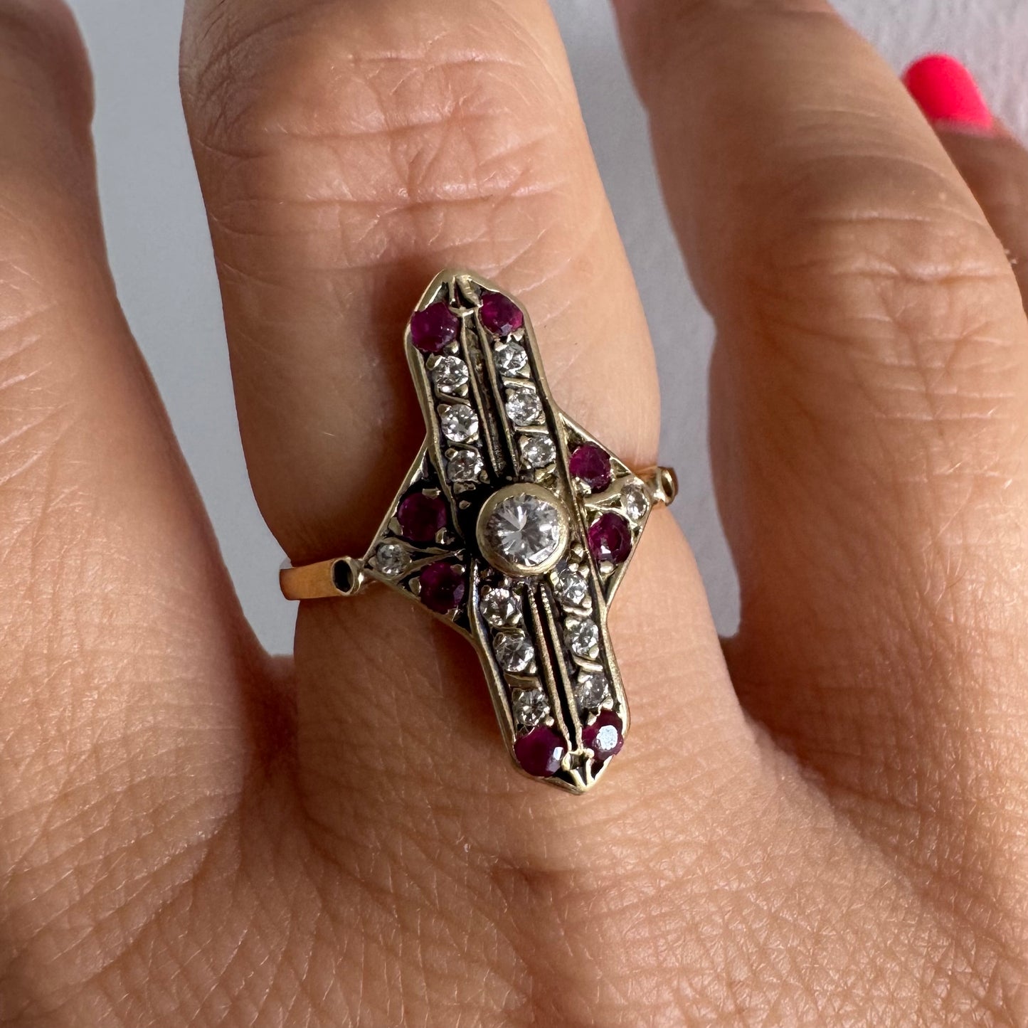 18K gold ring featuring a striking geometric design, set with a central Diamond surrounded by sparkling Diamonds and rich red Rubies.
