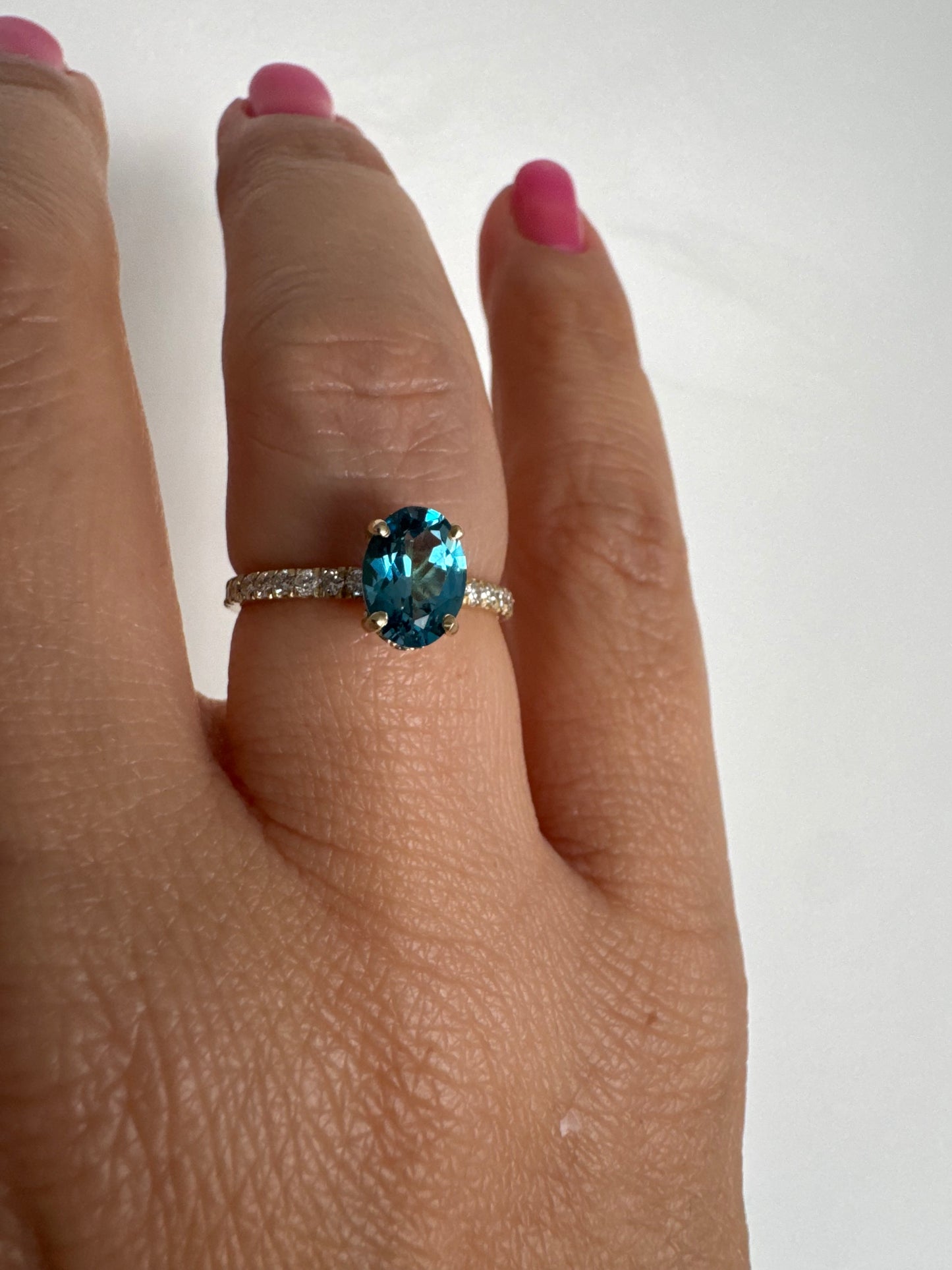 טבעת זהב צהוב 14 קראט משובצת אבן טופז כחולה אובלית בגוון טורקיז־כחול עמוק, באחיזה של ארבע שיניים עדינות ויהלומים.