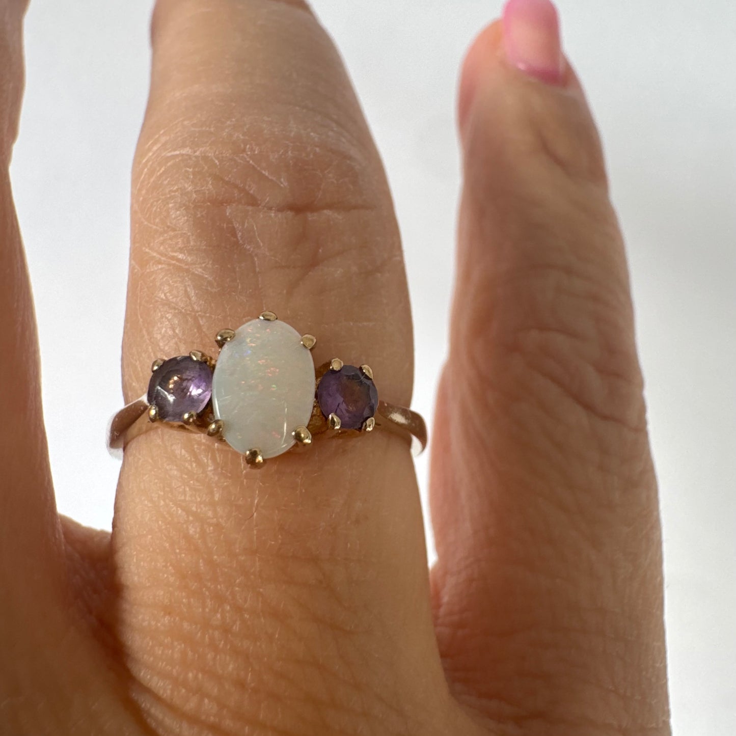 9K gold ring set with an oval Opal at the center, flanked by two delicate purple stones.
