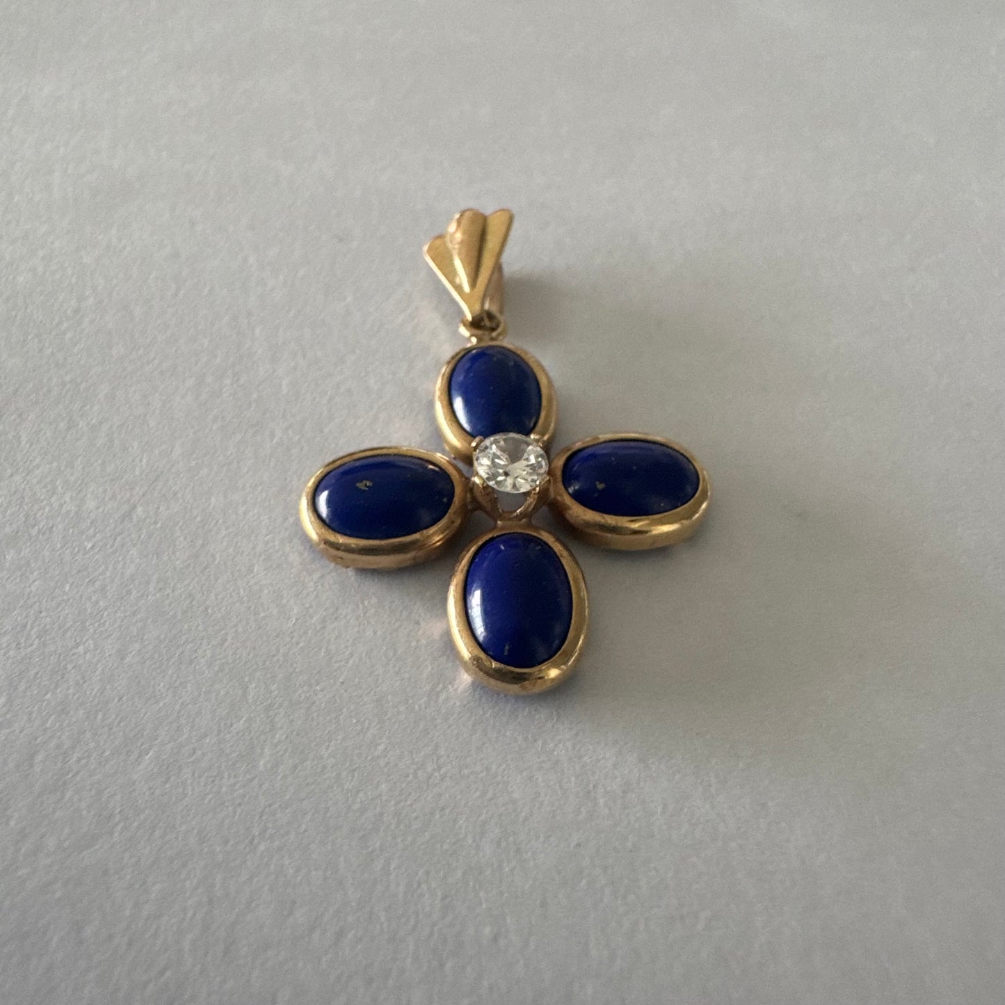 תליון זהב צהוב 14 קראט בעיצוב פרח סימטרי, משובץ ארבע אבני לפיס לזולי בגימור קבושון אובלי ובמרכזן יהלום עגול בוהק.