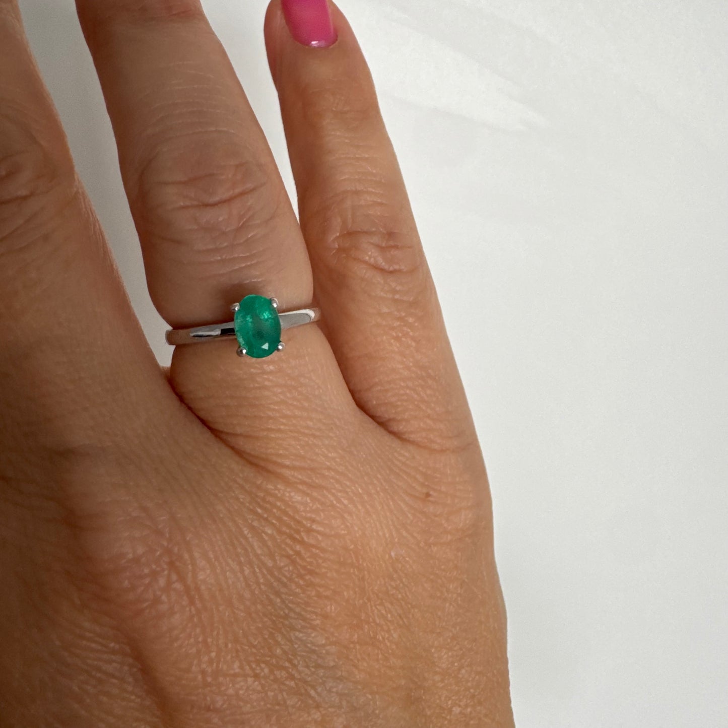 טבעת זהב לבן 14 קראט משובצת אבן אמרלד אובלית בגוון ירוק עשיר.