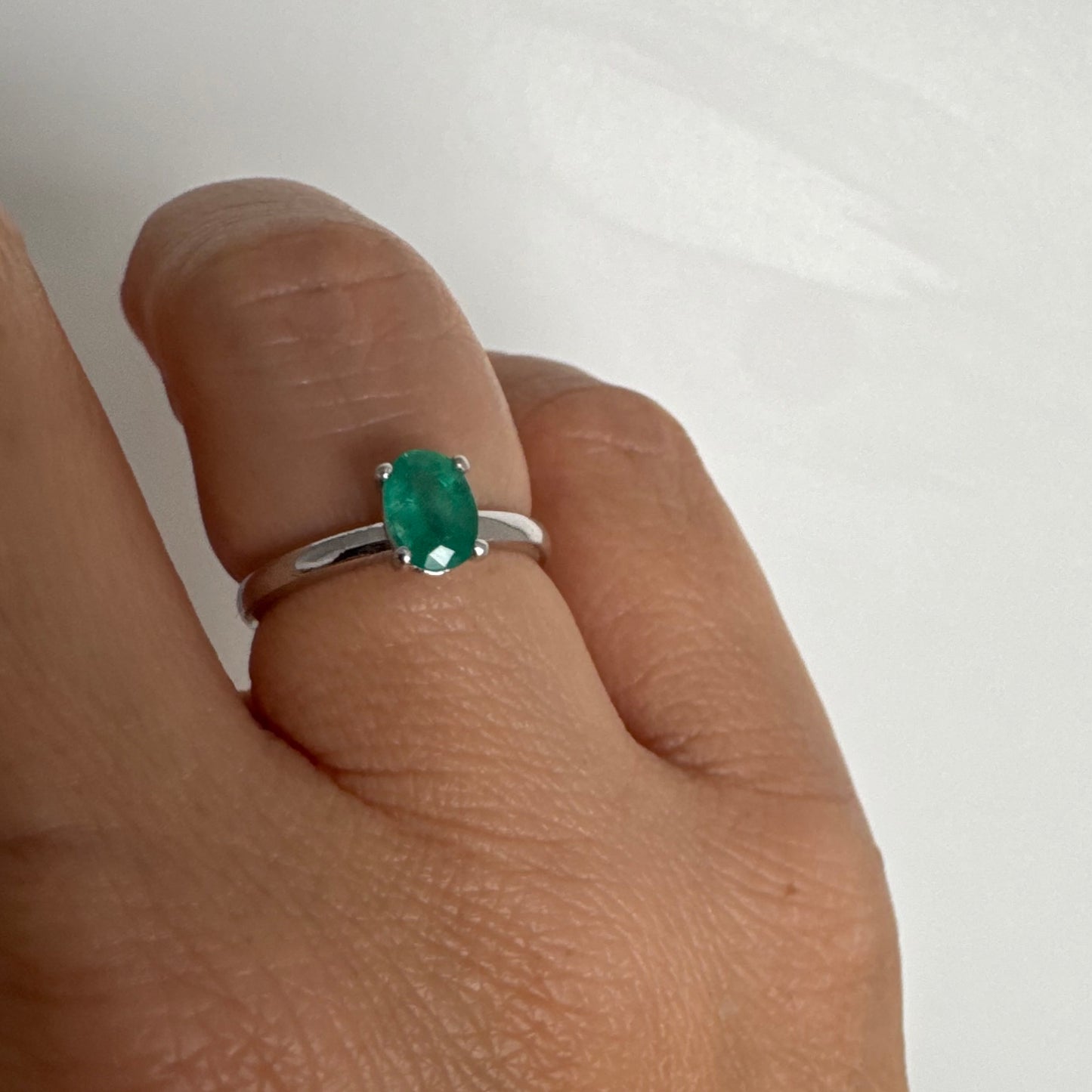 טבעת זהב לבן 14 קראט משובצת אבן אמרלד אובלית בגוון ירוק עשיר.