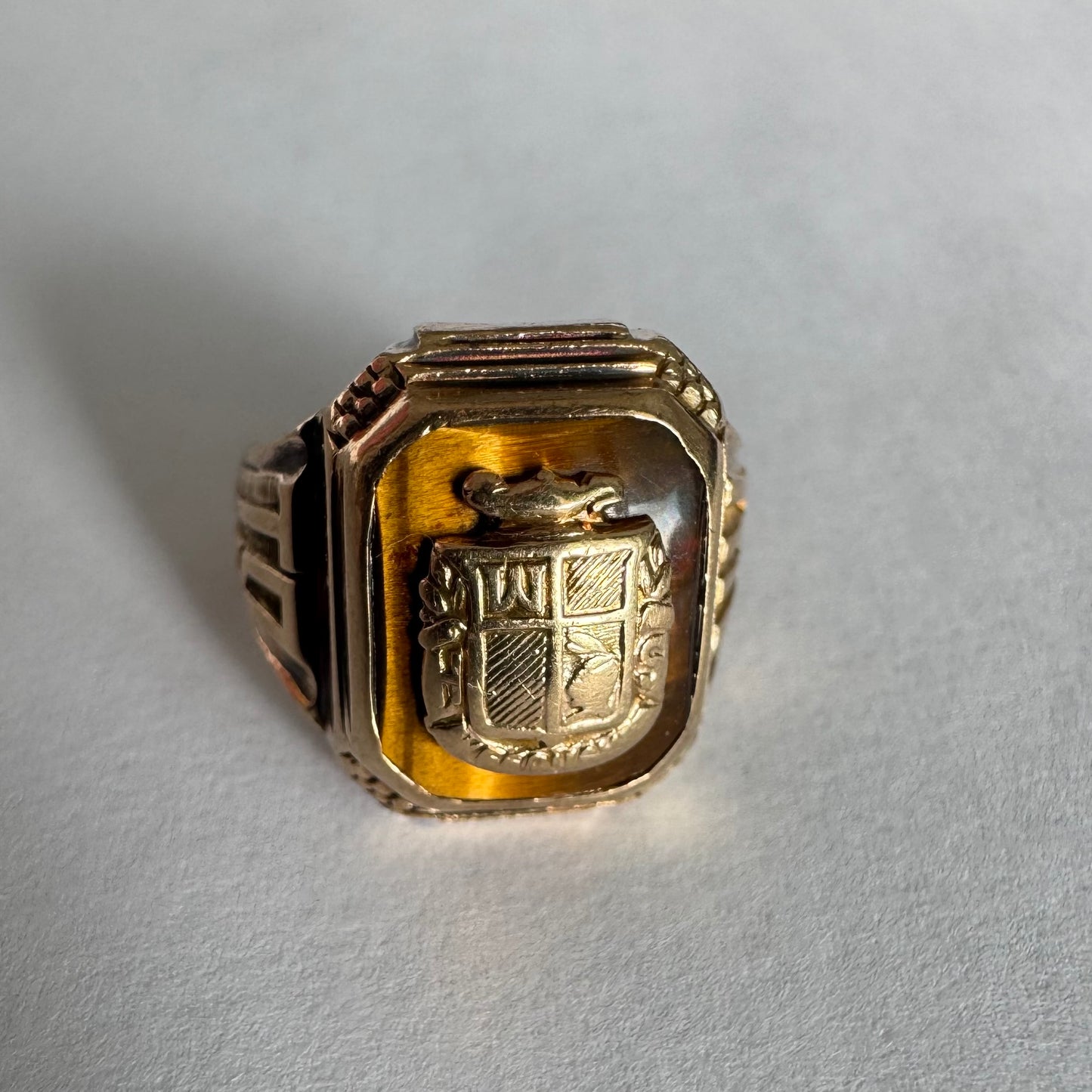 טבעת חותם זהב צהוב 10 קראט עם אבן בגוון חום-דבש ועיטור סמל מובלט במרכז.