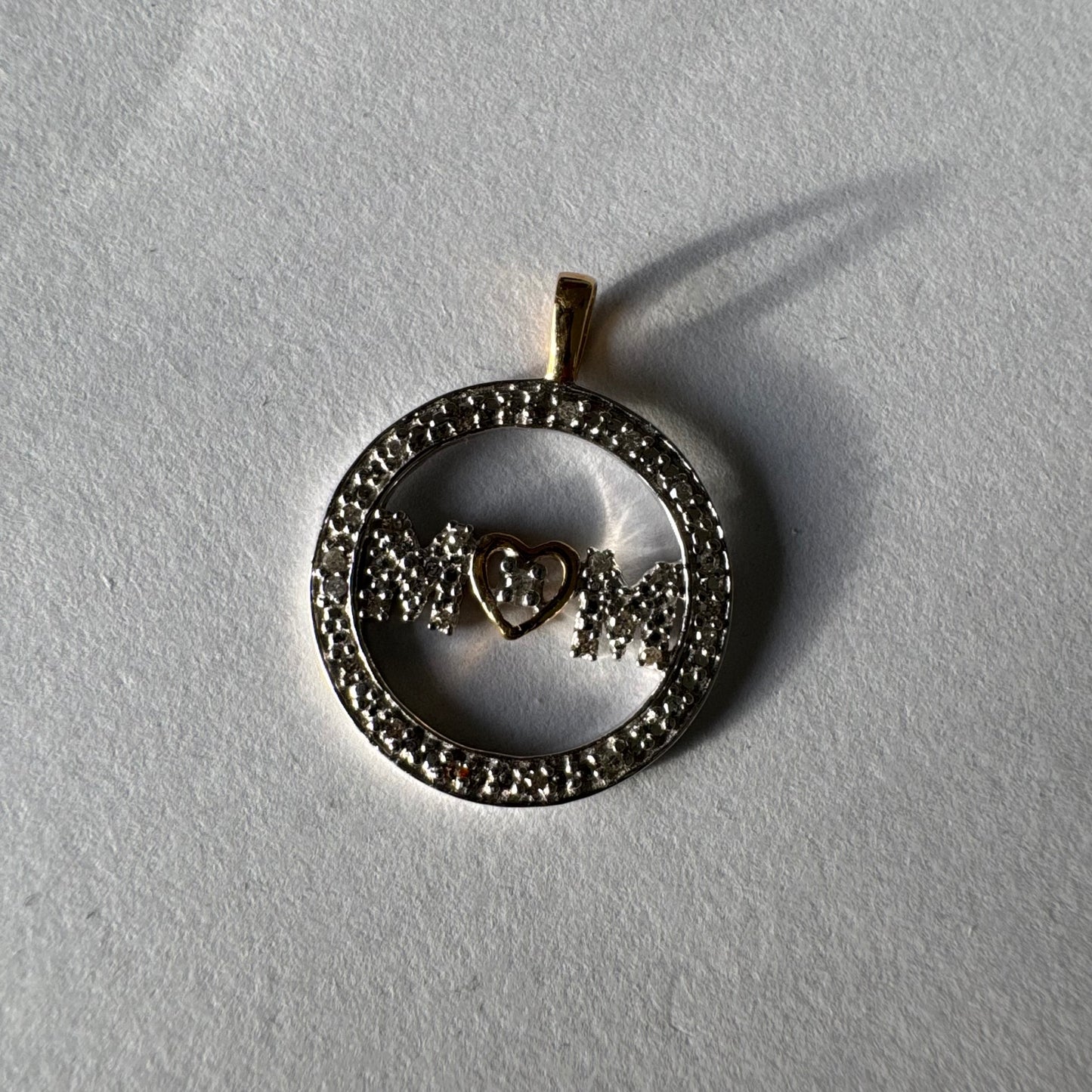 תליון זהב לבן 14 קראט עם הכיתוב ״MOM” מוקף מסגרת יהלומים עדינה.