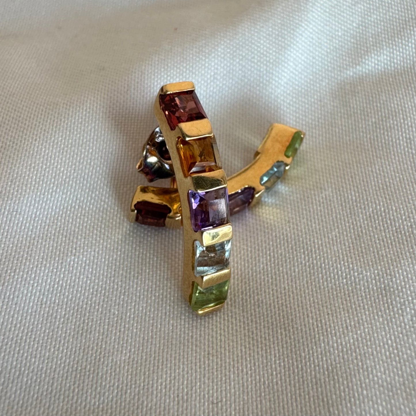 18K gold hoop earrings set with a vibrant line of multi-colored gemstones — including Garnet, Citrine, Amethyst, Peridot, and Blue Topaz.