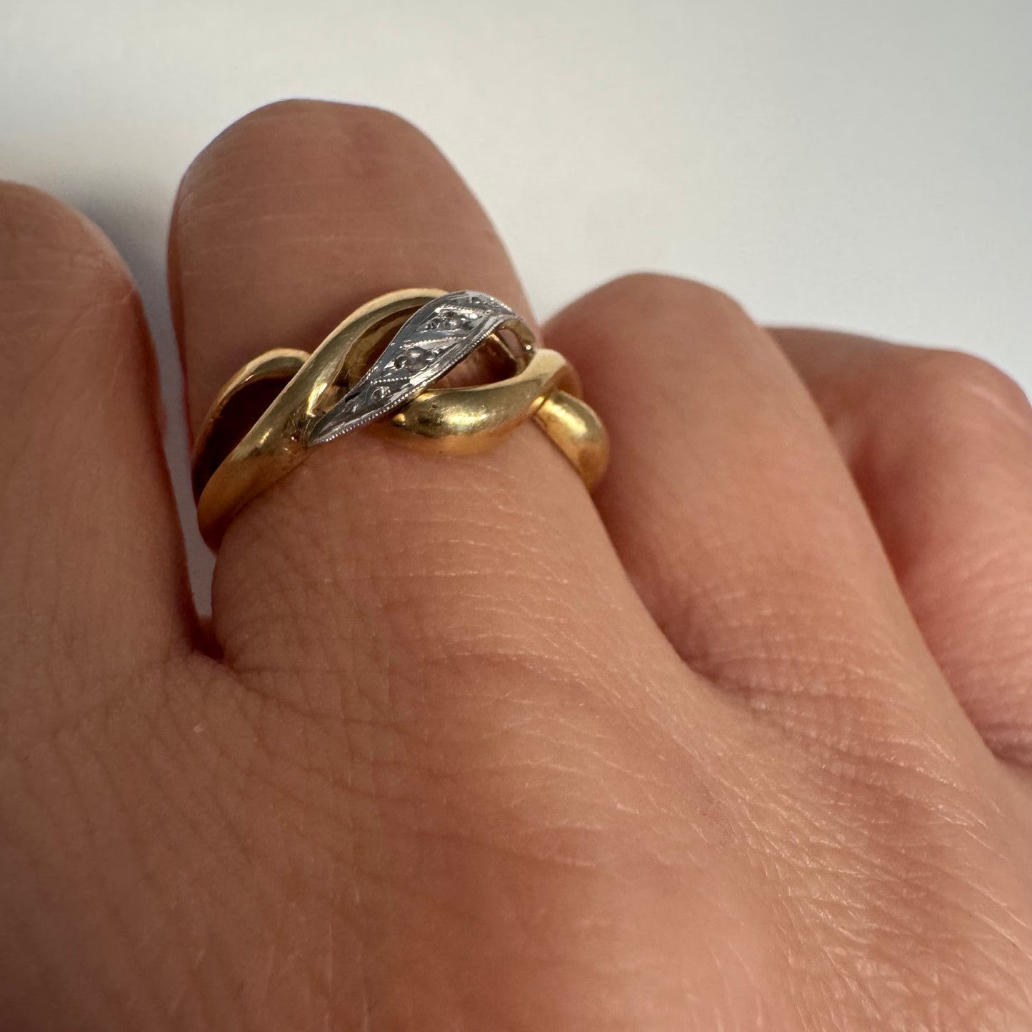 טבעת זהב צהוב 18 קראט בעיצוב קשר קלאסי, בשילוב אלמנט מרכזי מזהב לבן משובץ יהלומים עדינים.