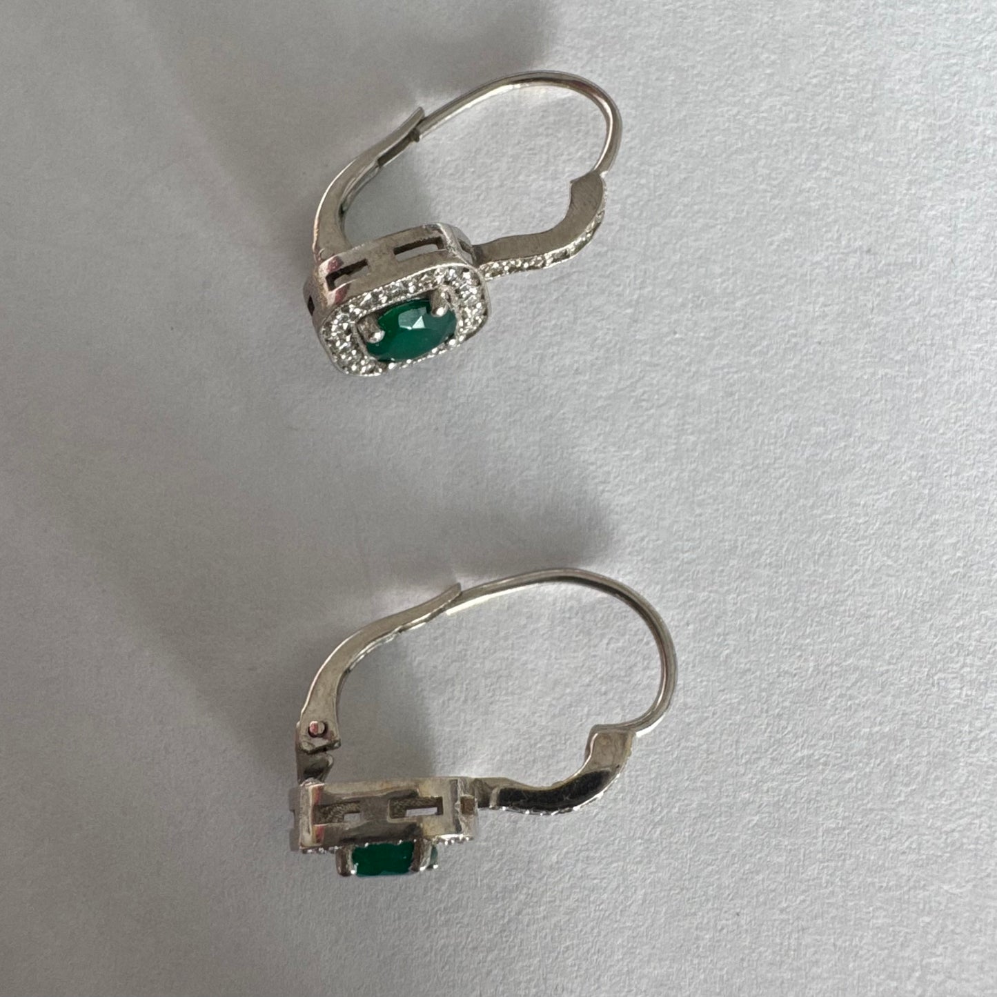 עגילי זהב לבן 14 קראט בעיצוב אלגנטי ונקי, משובצים אבן אמרלד מרכזית במראה עשיר ועמוק, מוקפת הילה מנצנצת של יהלומים.