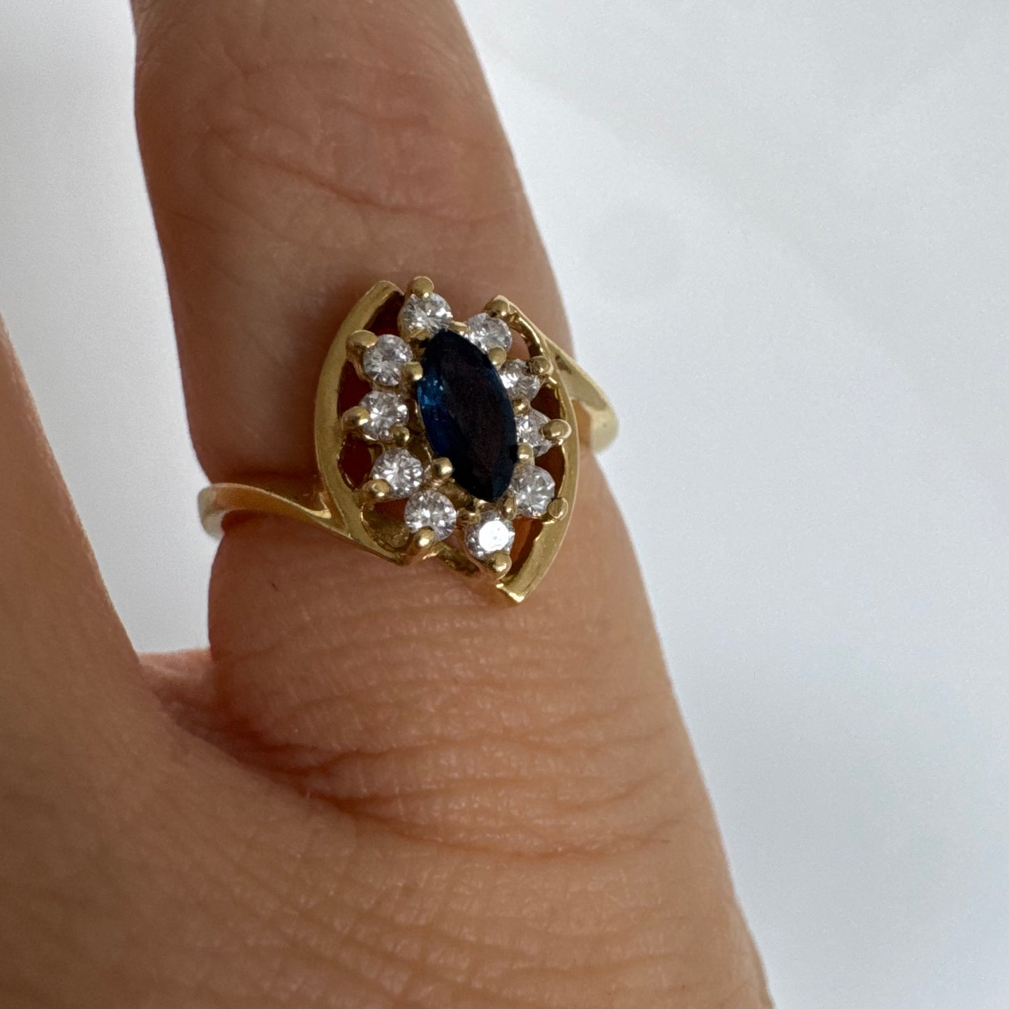 טבעת זהב צהוב 18 קראט משובצת ספיר כחול מרכזי בחיתוך מרקיזה, מוקף הילה של יהלומים המעניקים ניצוץ עדין ומדגישים את צבע האבן העמוק.