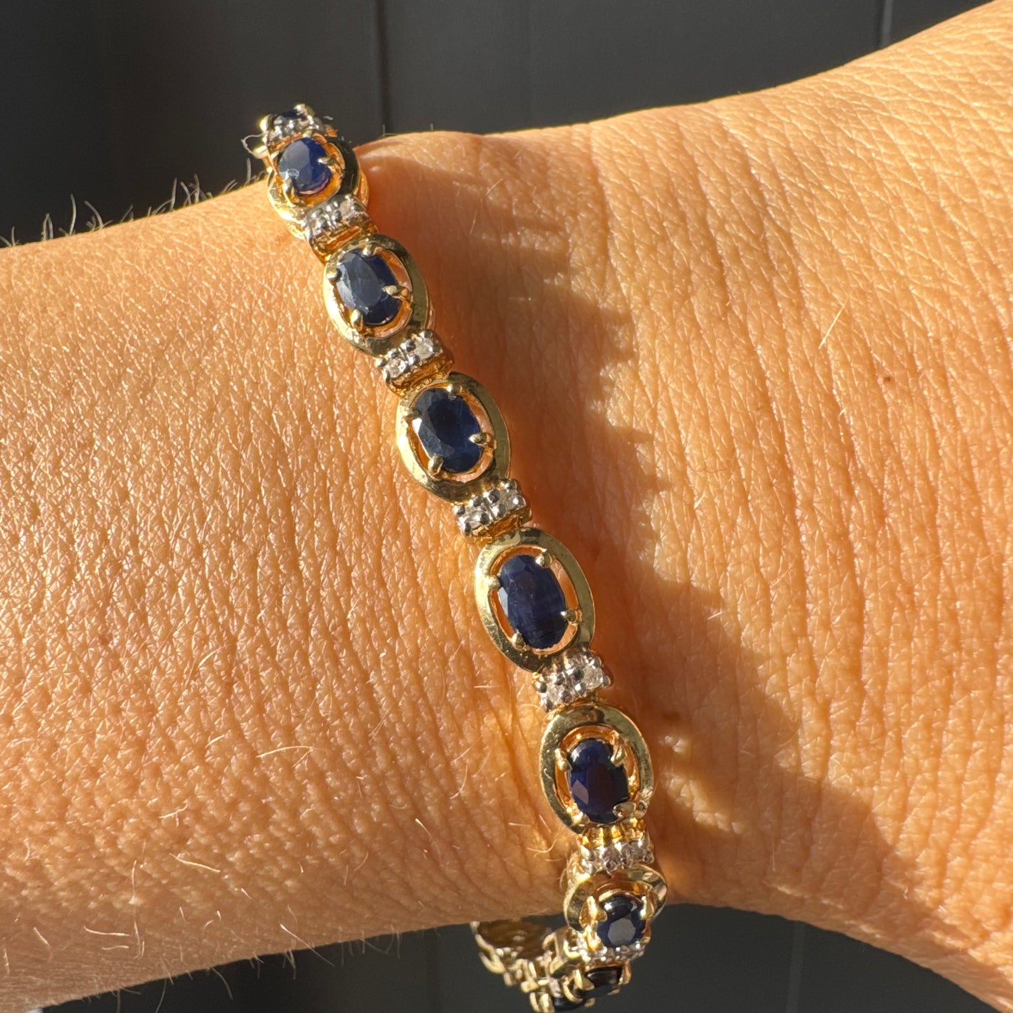 צמיד זהב צהוב 10 קראט בעיצוב קלאסי ועשיר, משובץ אבני ספיר אובליות בגוון כחול עמוק וביניהן שיבוצי יהלומים לבנים עדינים.