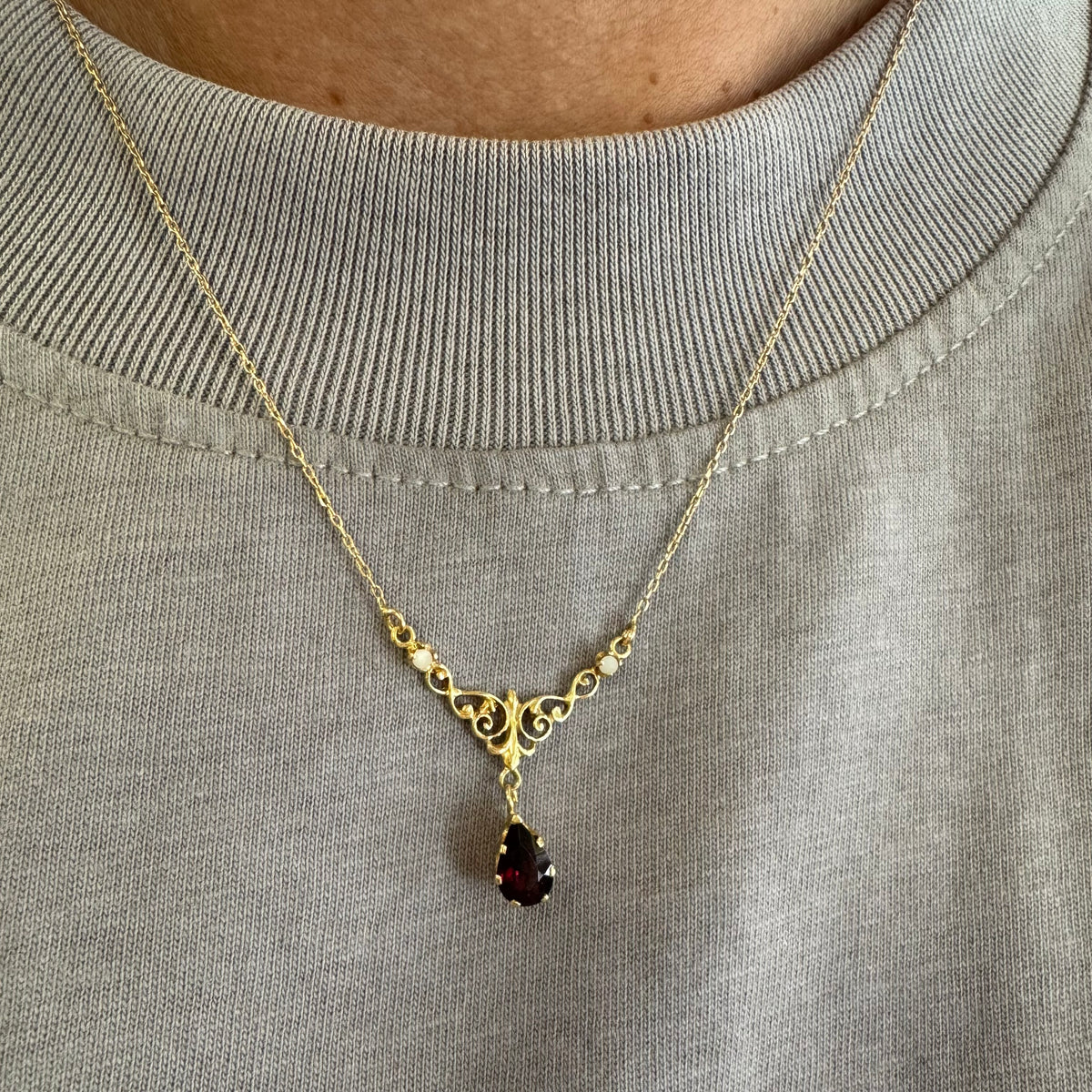 18K gold Necklace featuring an elegant scrollwork design and a striking deep-red pear-shaped Garnet drop.
