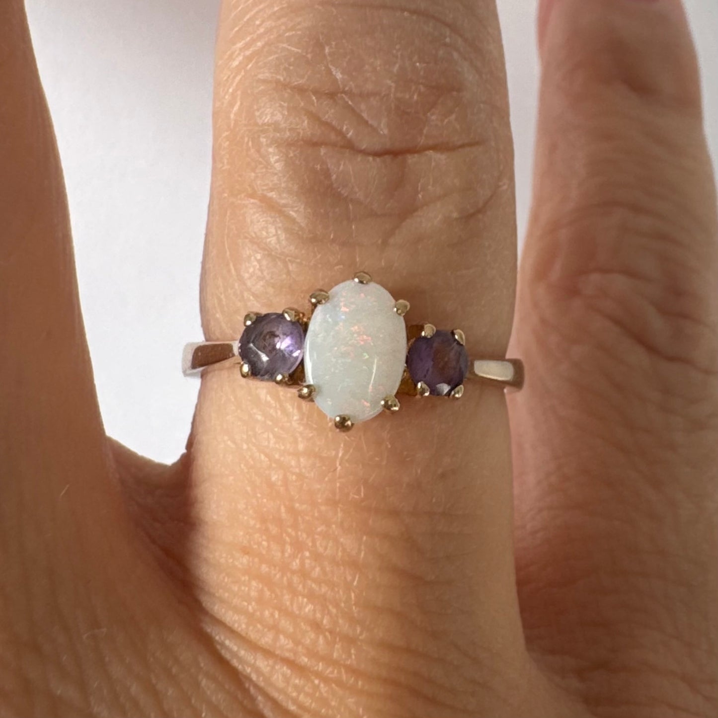 9K gold ring set with an oval Opal at the center, flanked by two delicate purple stones.