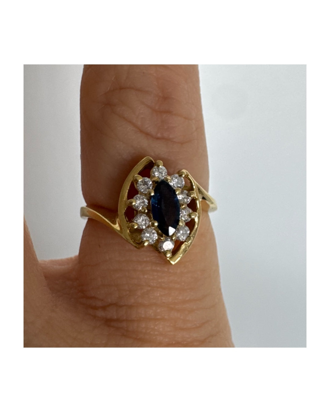 טבעת זהב צהוב 18 קראט משובצת ספיר כחול מרכזי בחיתוך מרקיזה, מוקף הילה של יהלומים המעניקים ניצוץ עדין ומדגישים את צבע האבן העמוק.