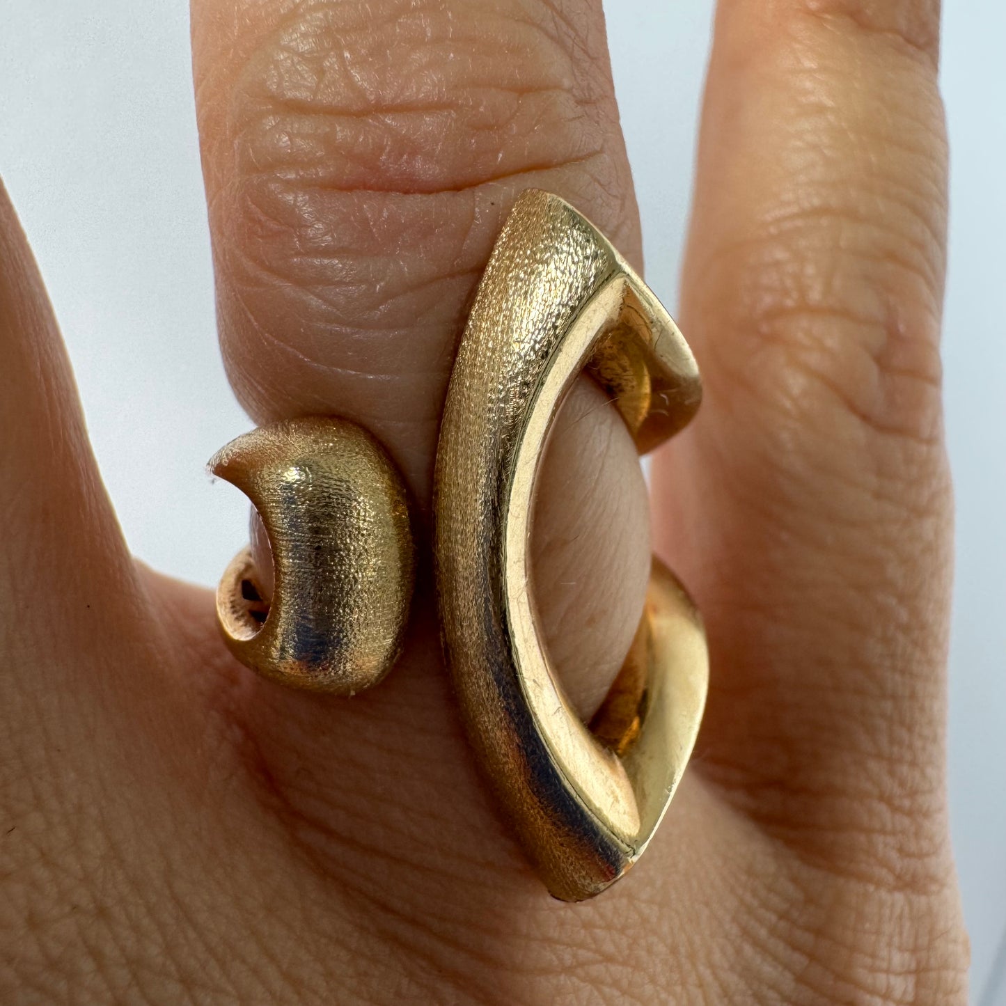 14K gold sculptural ring with a bold, modern design featuring flowing, asymmetrical lines.