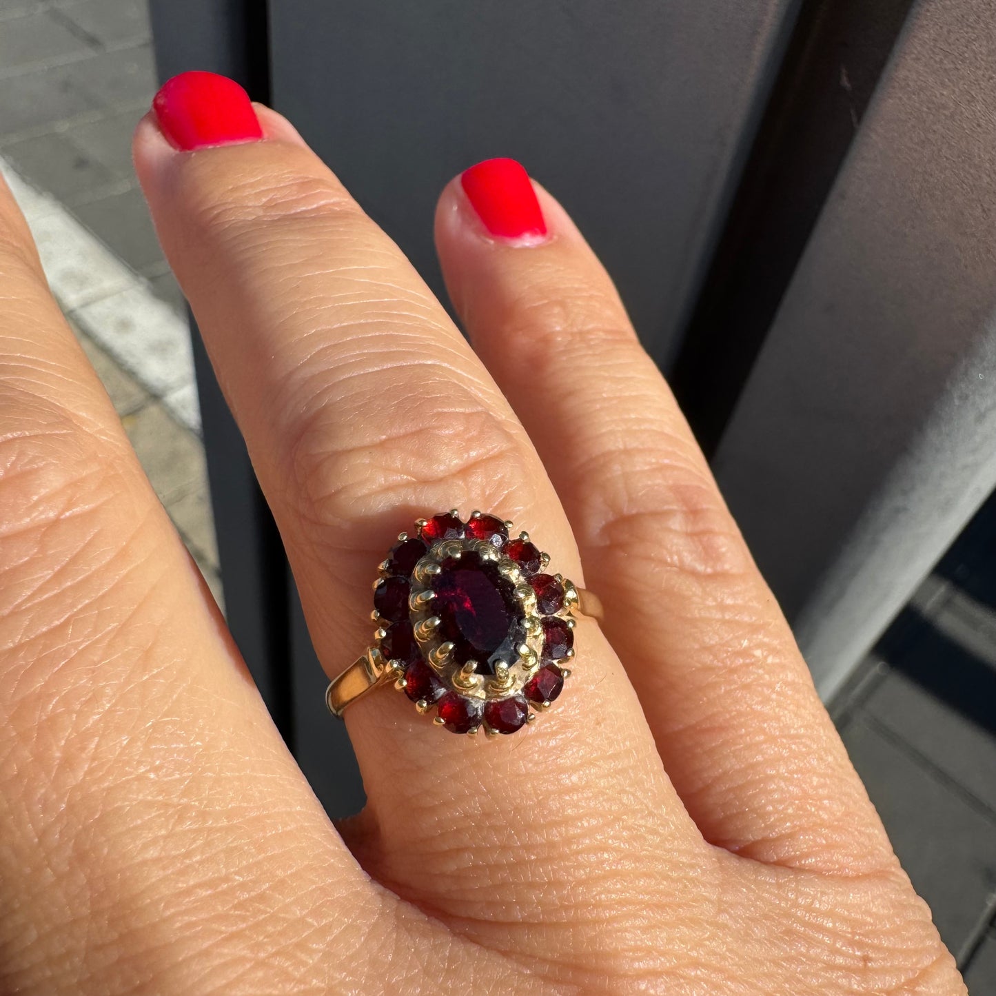 טבעת זהב צהוב 18 קראט משובצת אבן גרנט אובלית במרכז, מוקפת באבני גרנט קטנות בסידור אליפטי קלאסי.