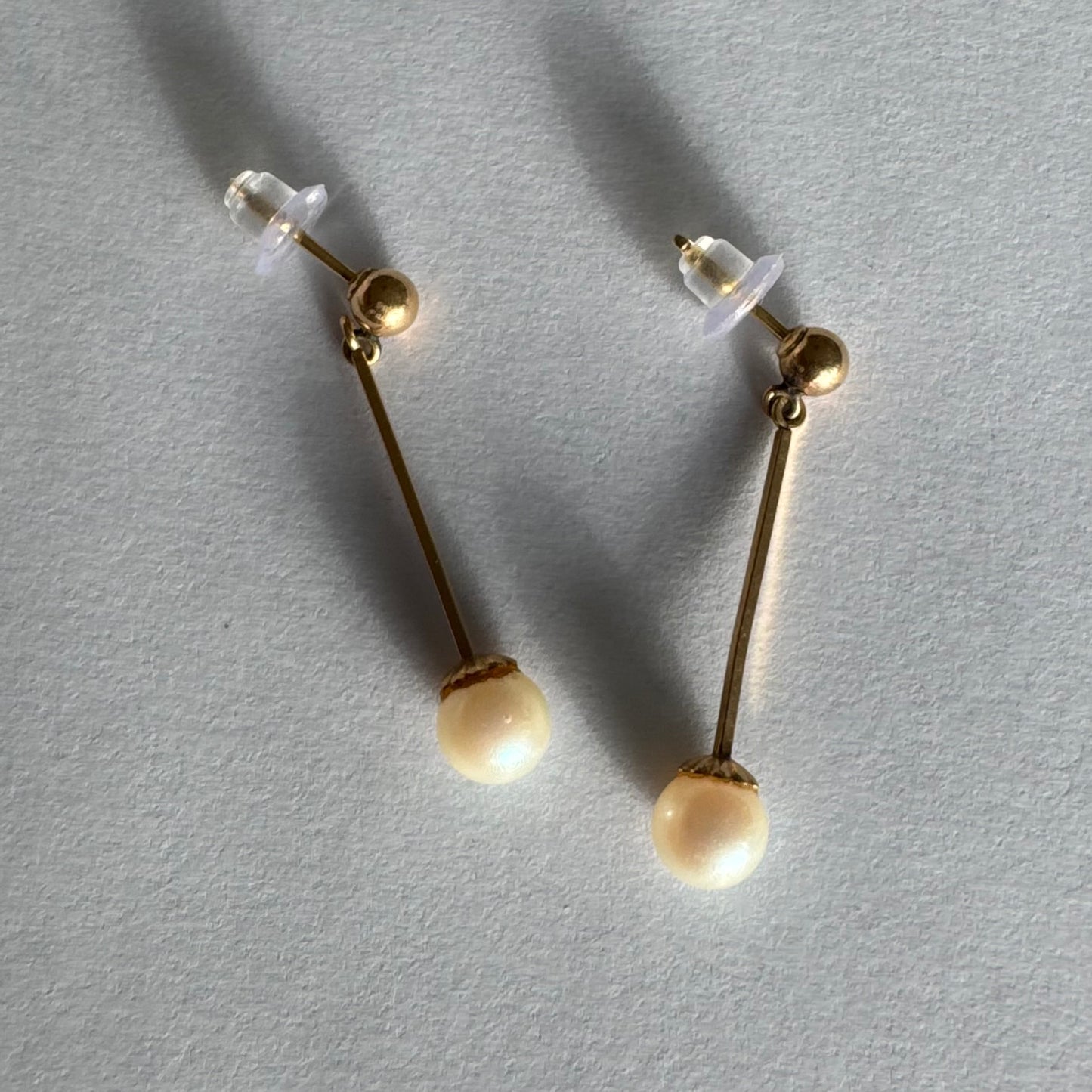 עגילי זהב 14 קראט בעיצוב תלוי ועדין, עם פנינה עגולה בקצה.