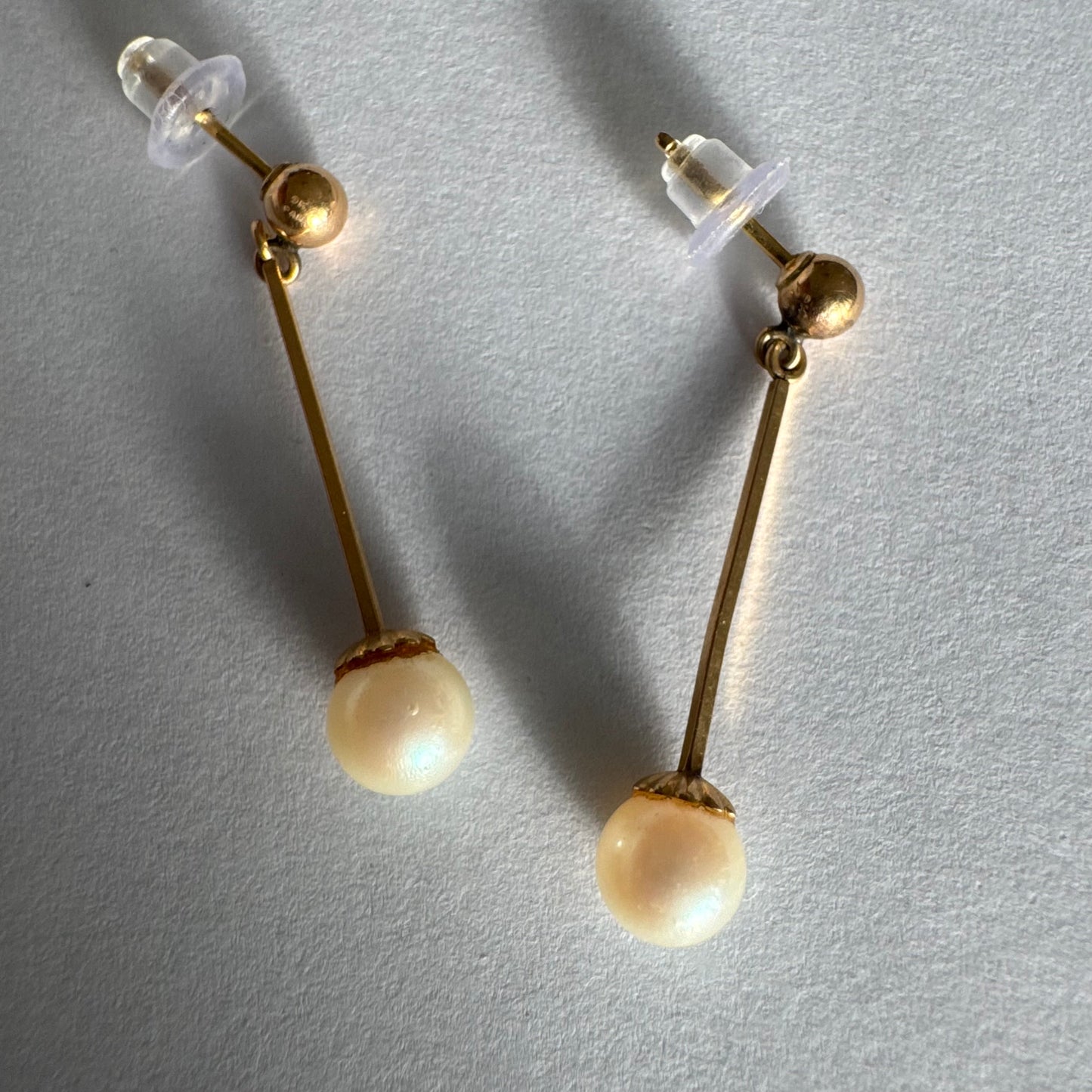 עגילי זהב 14 קראט בעיצוב תלוי ועדין, עם פנינה עגולה בקצה.