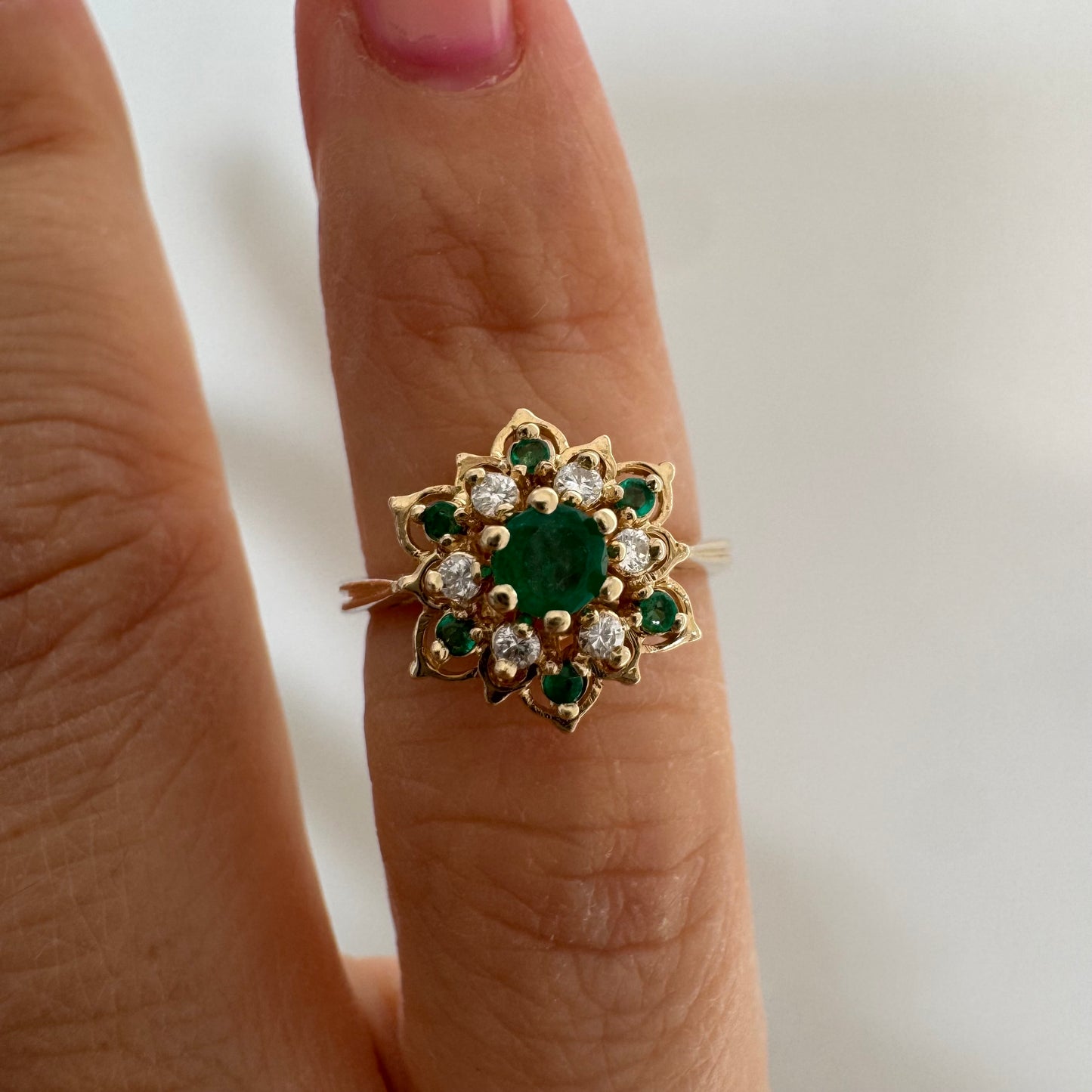 טבעת זהב 14 קראט בעיצוב פרח משובצת אבן אמרלד מרכזית, מוקפת יהלומים ואבני אמרלד נוספות