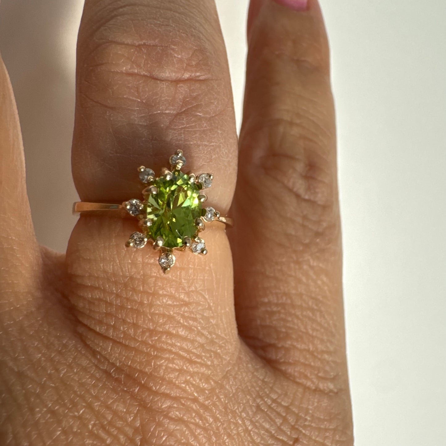 טבעת זהב 14 קראט משובצת אבן פרידוט ירוקה בחיתוך אובלי, מוקפת יהלומים היוצרים הילה עדינה מסביבה.